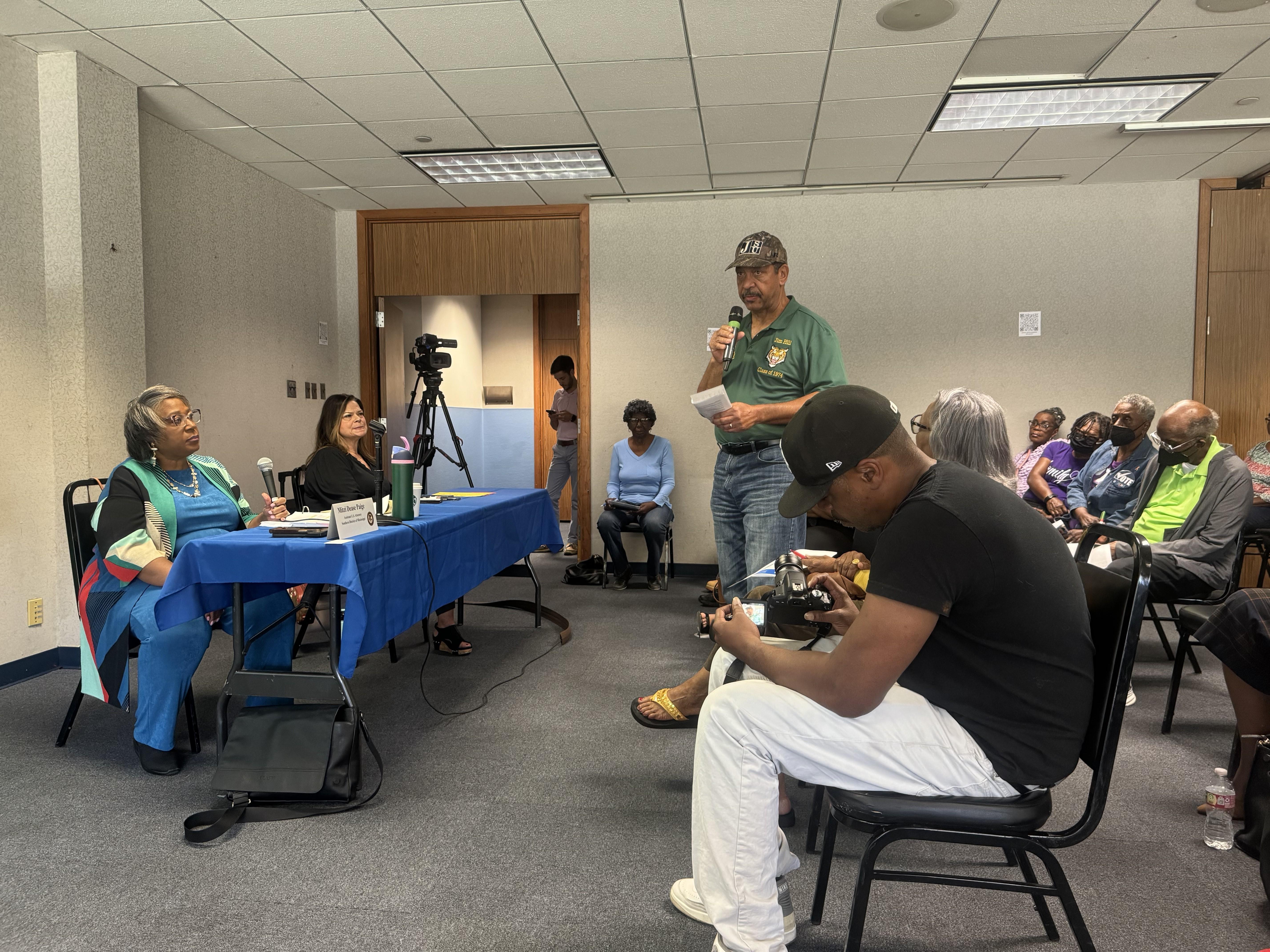 A Jackson resident stands before a room of other seated residents. He has a mic in his hand.