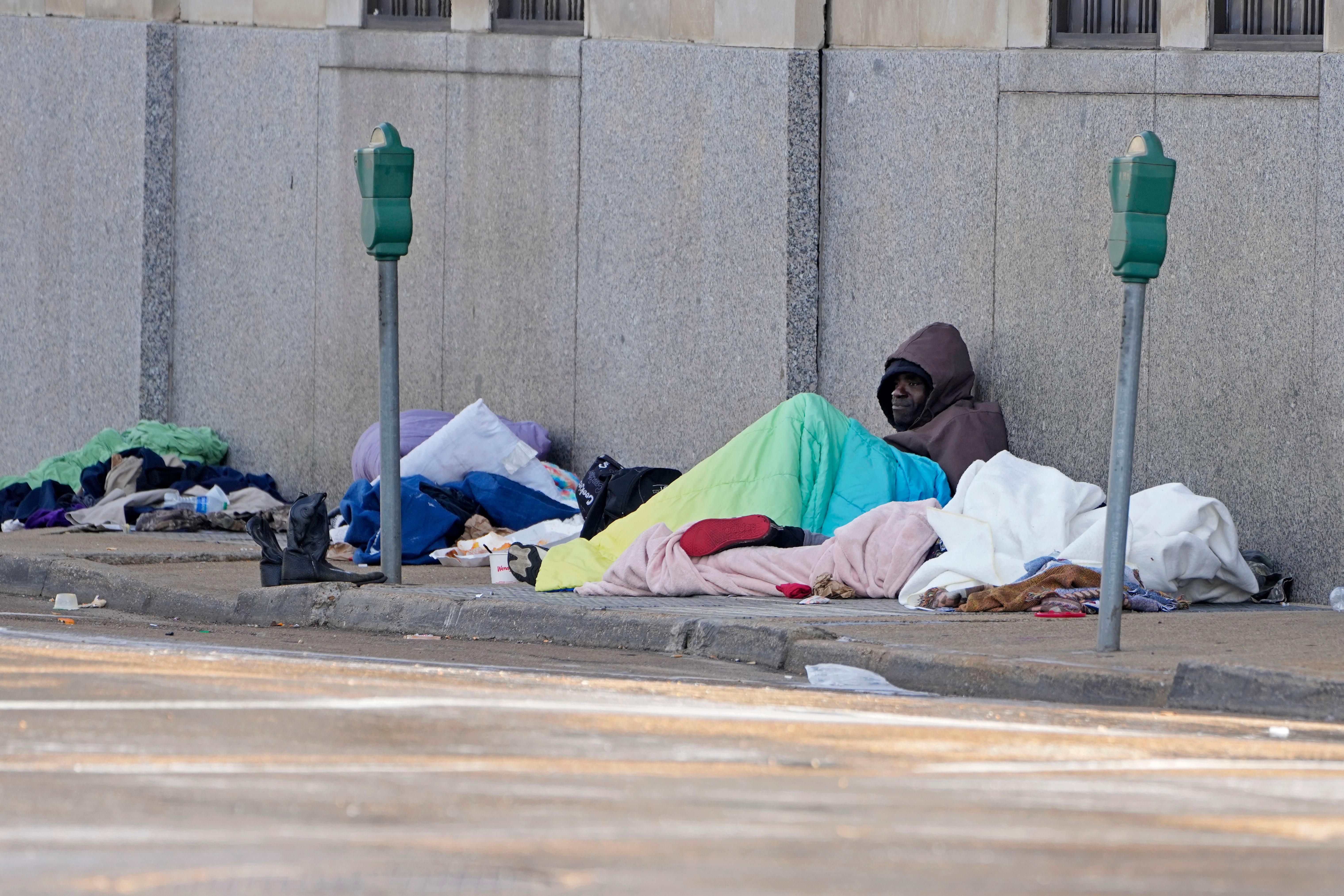 A man leans against a city wall trying to keep warm.