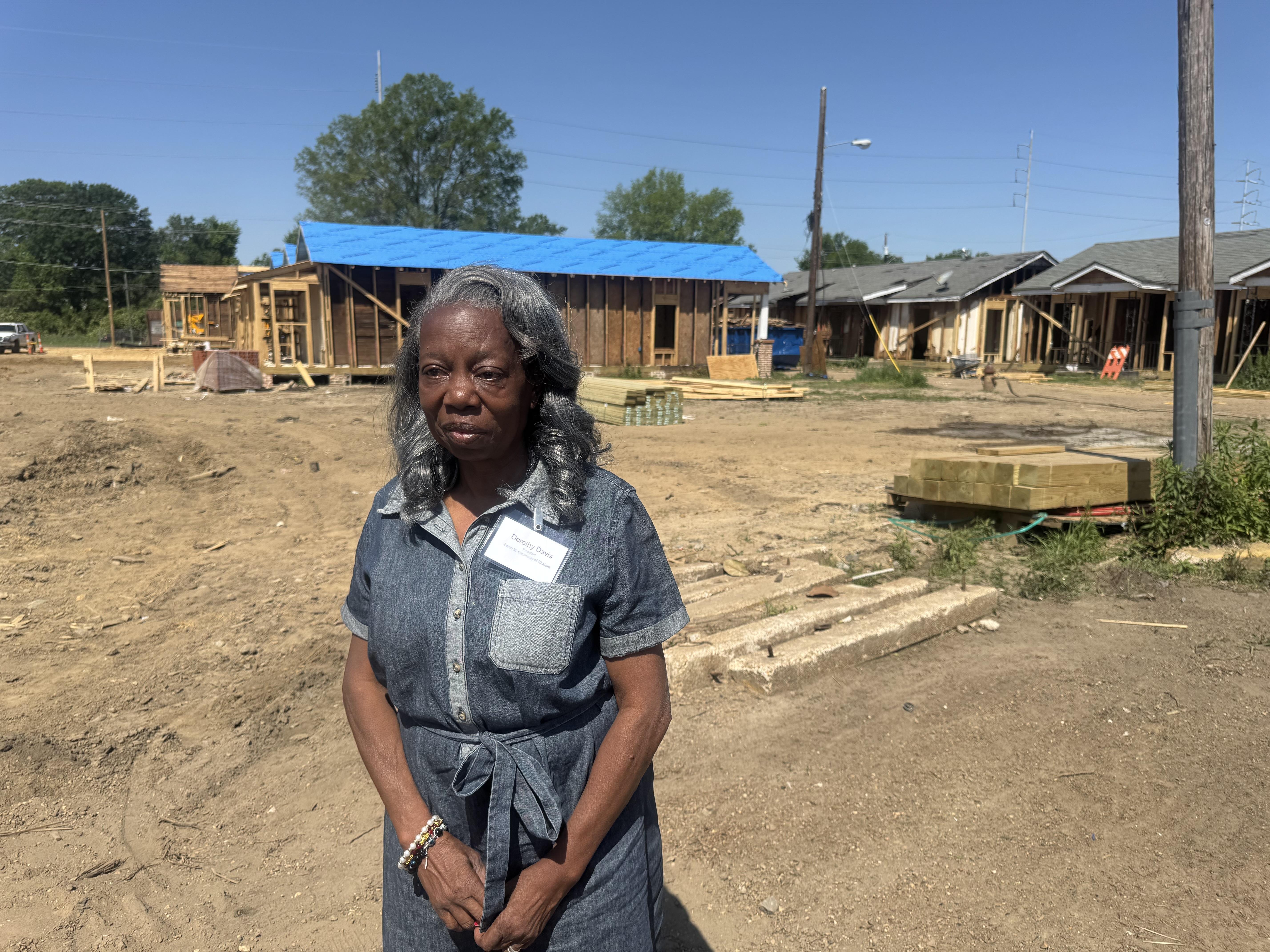 A woman looks off to the side as historic homes undergoing renovation are seen behind her.