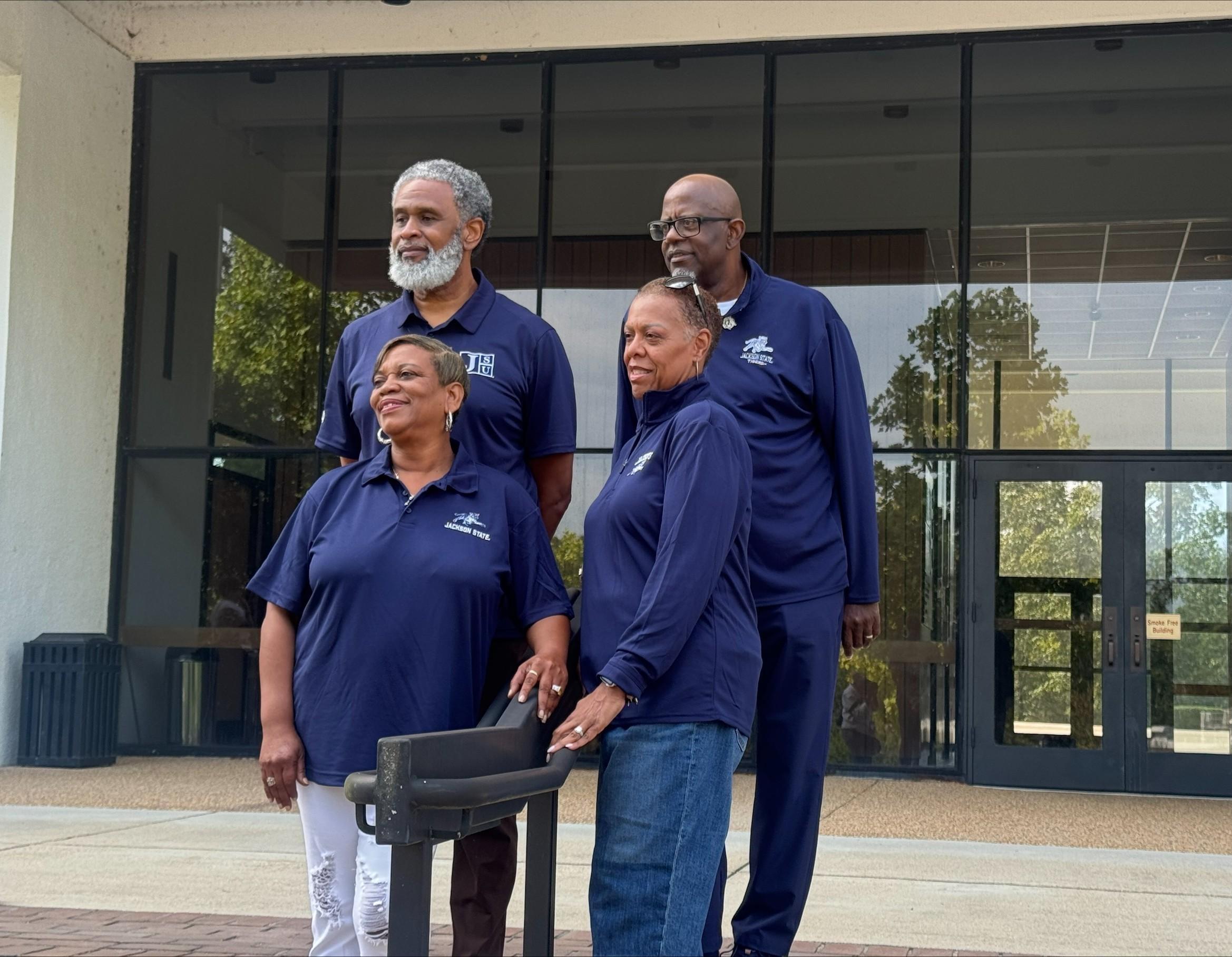 A group of four university alumni wear matching shirts and pose for a portrait. 