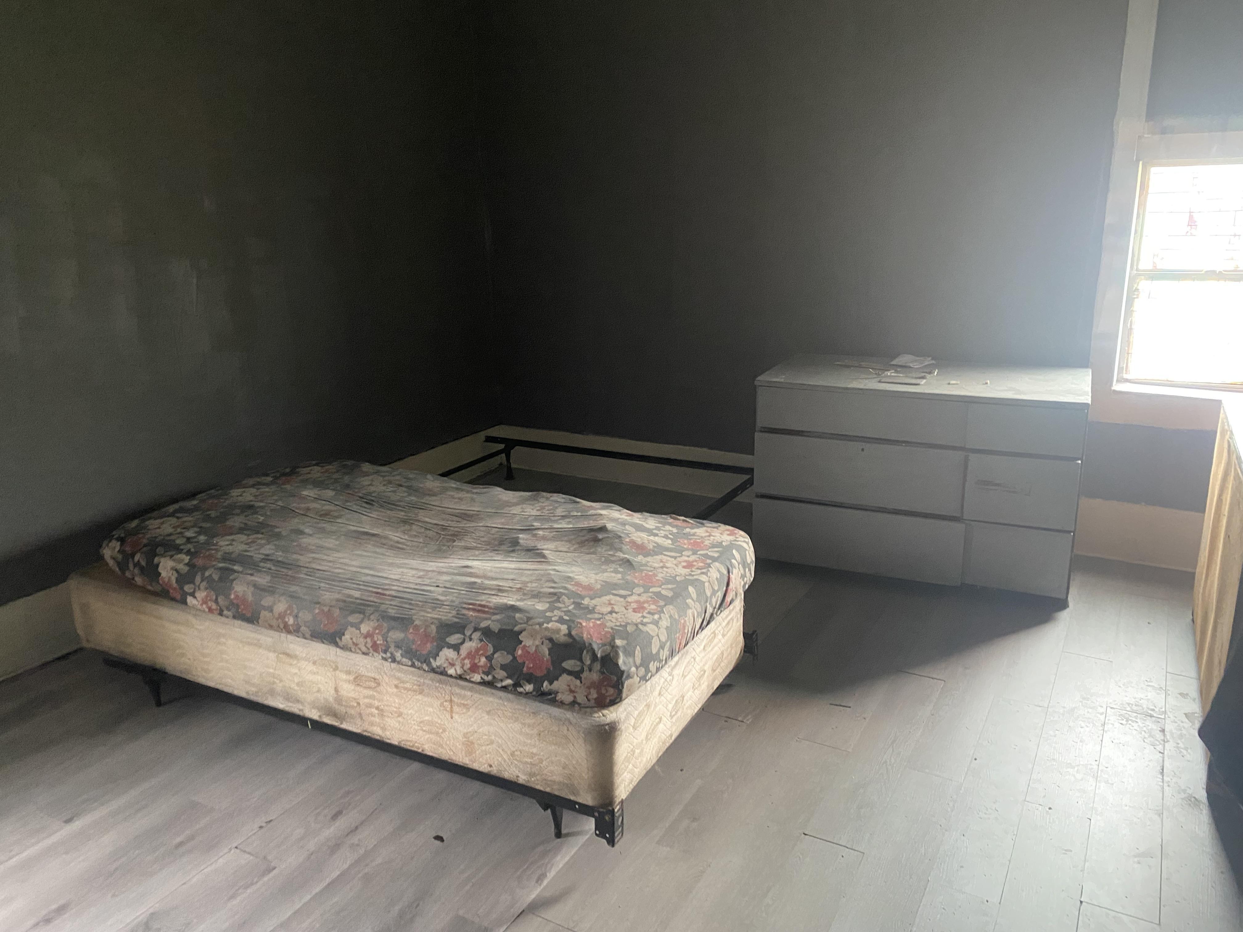 A barren bedroom with a floral mattress and broken dresser.