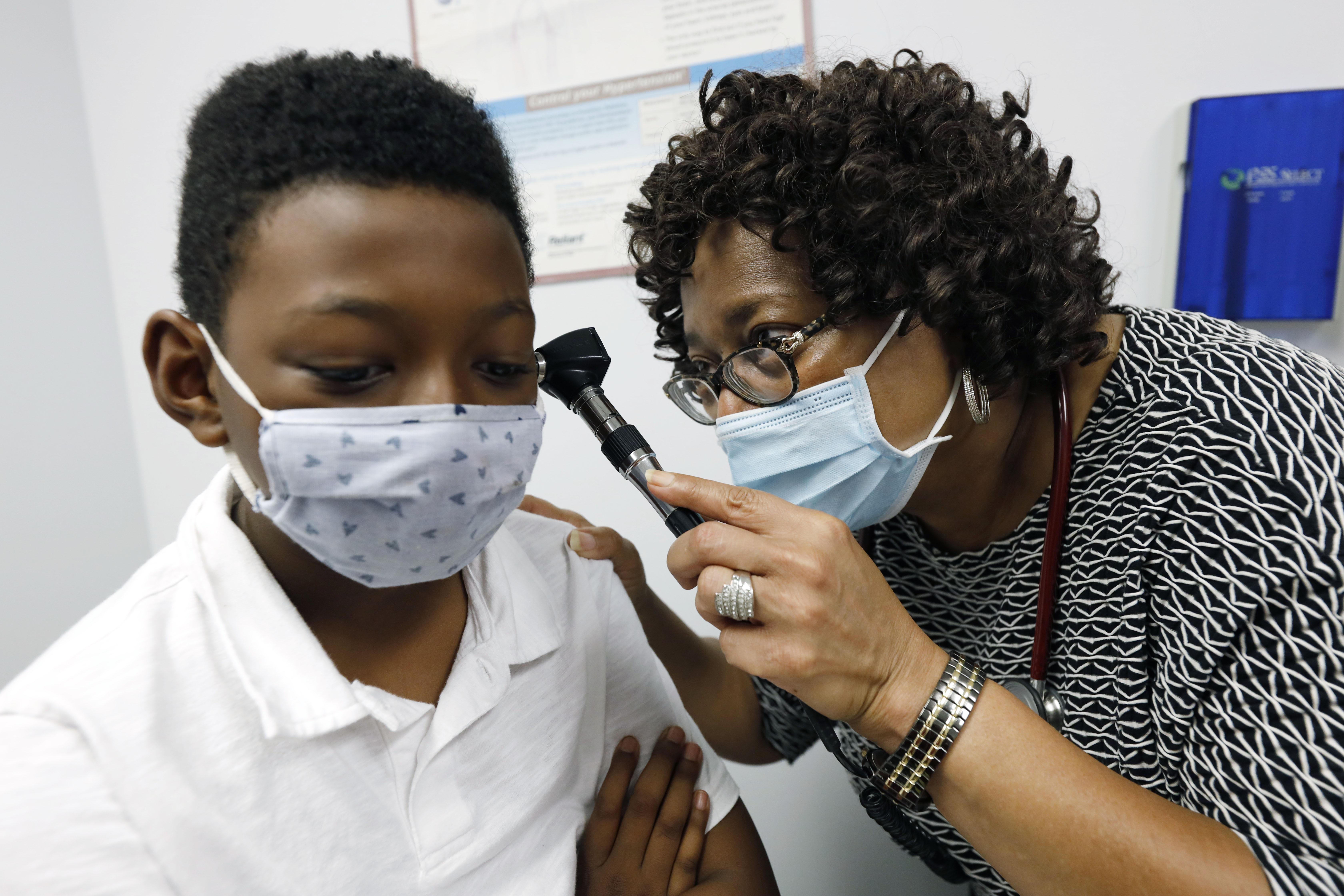 A Black doctor looks into the ear of a child