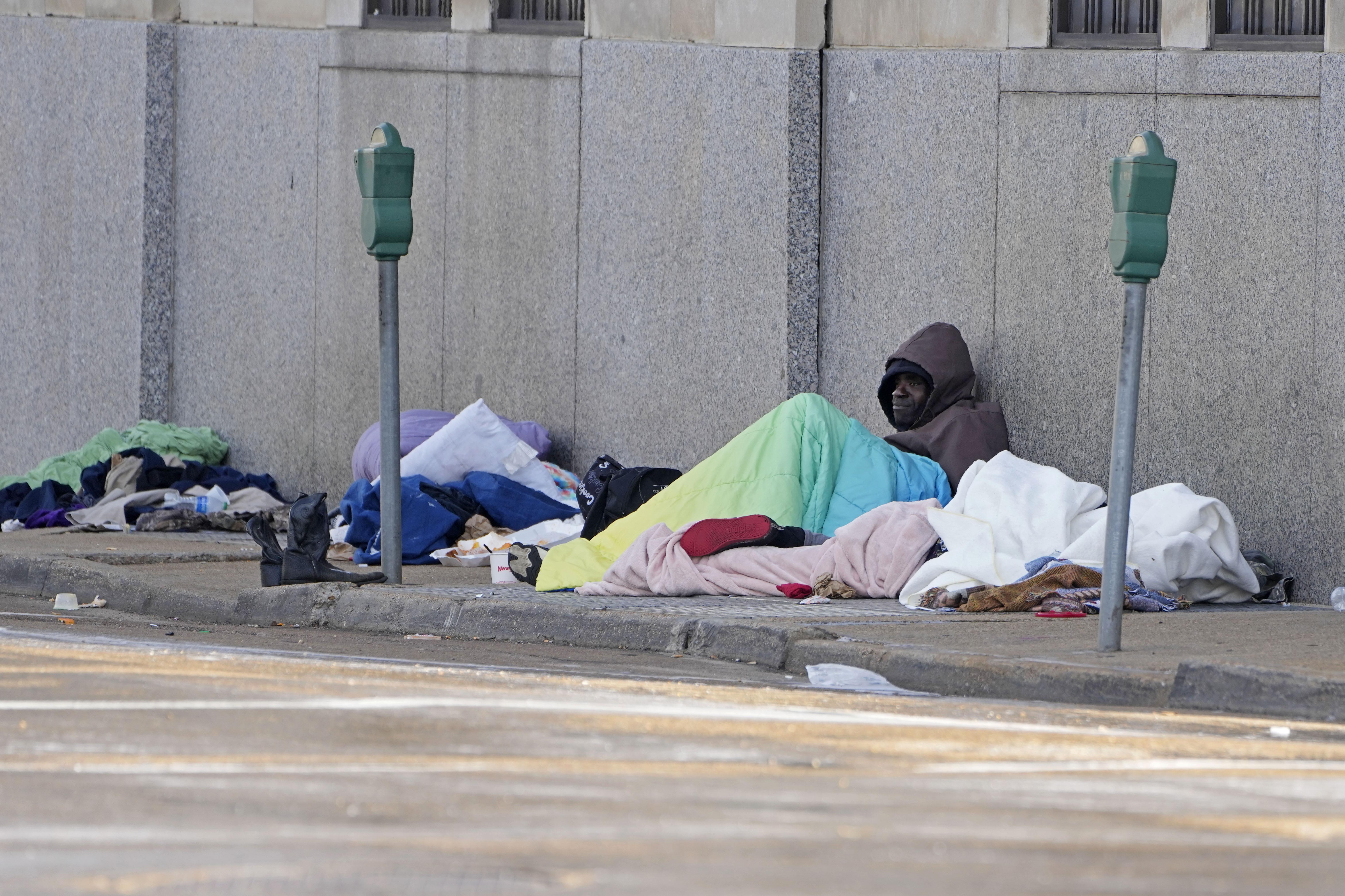 A man leans against a city wall trying to keep warm.