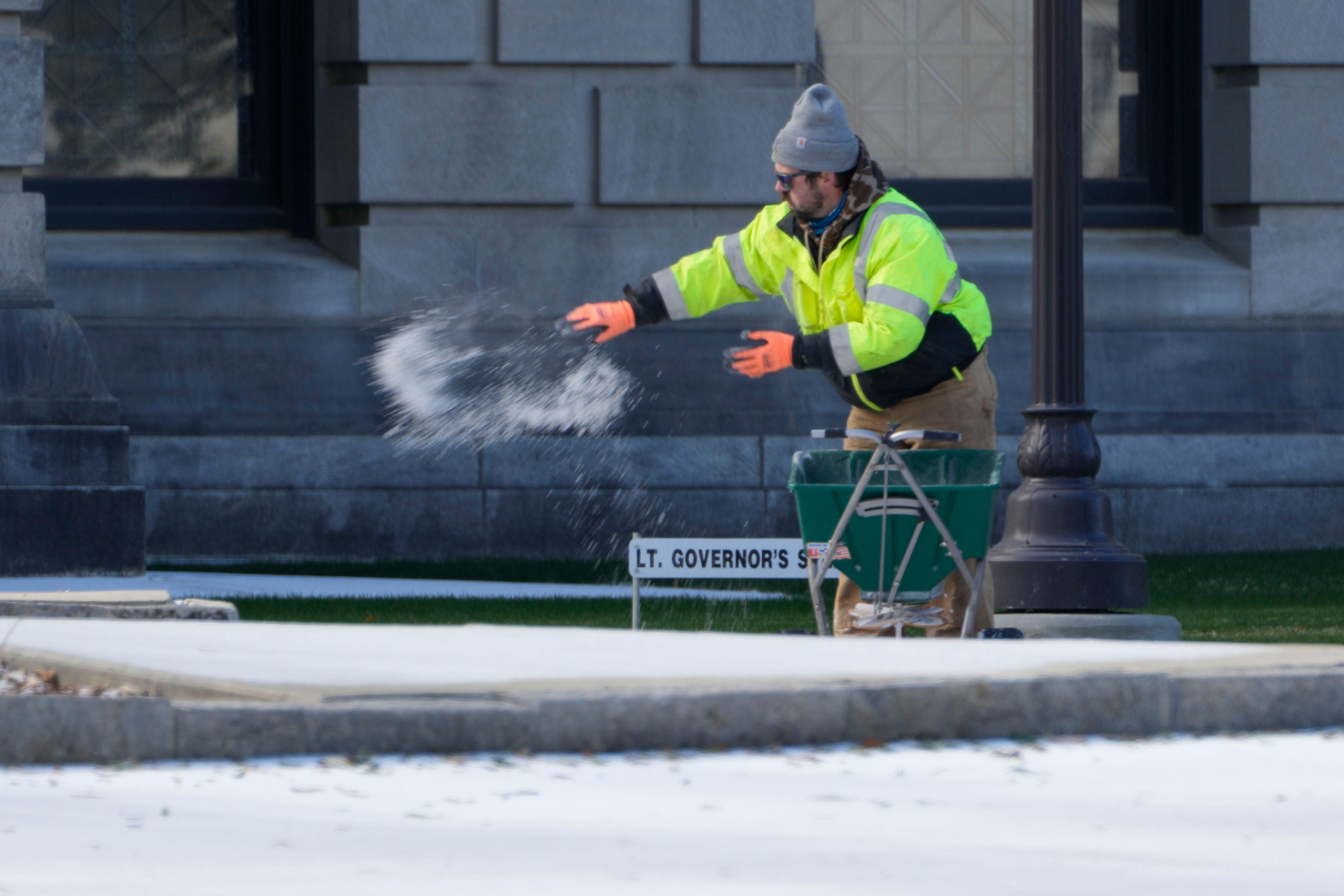 A man spreads ice melter across a sidewalk.