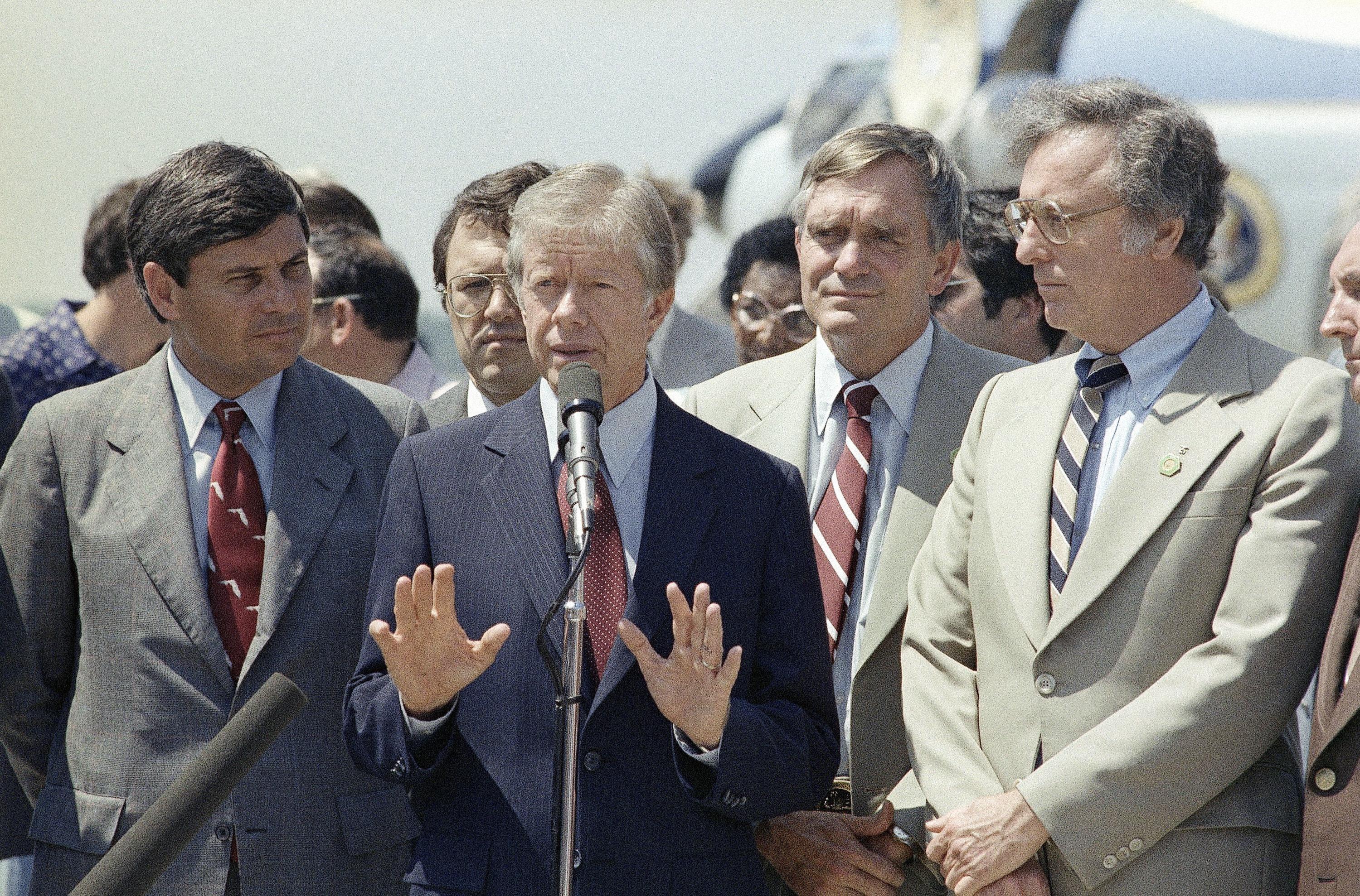 A man raises his hands as he speaks into a microphone.