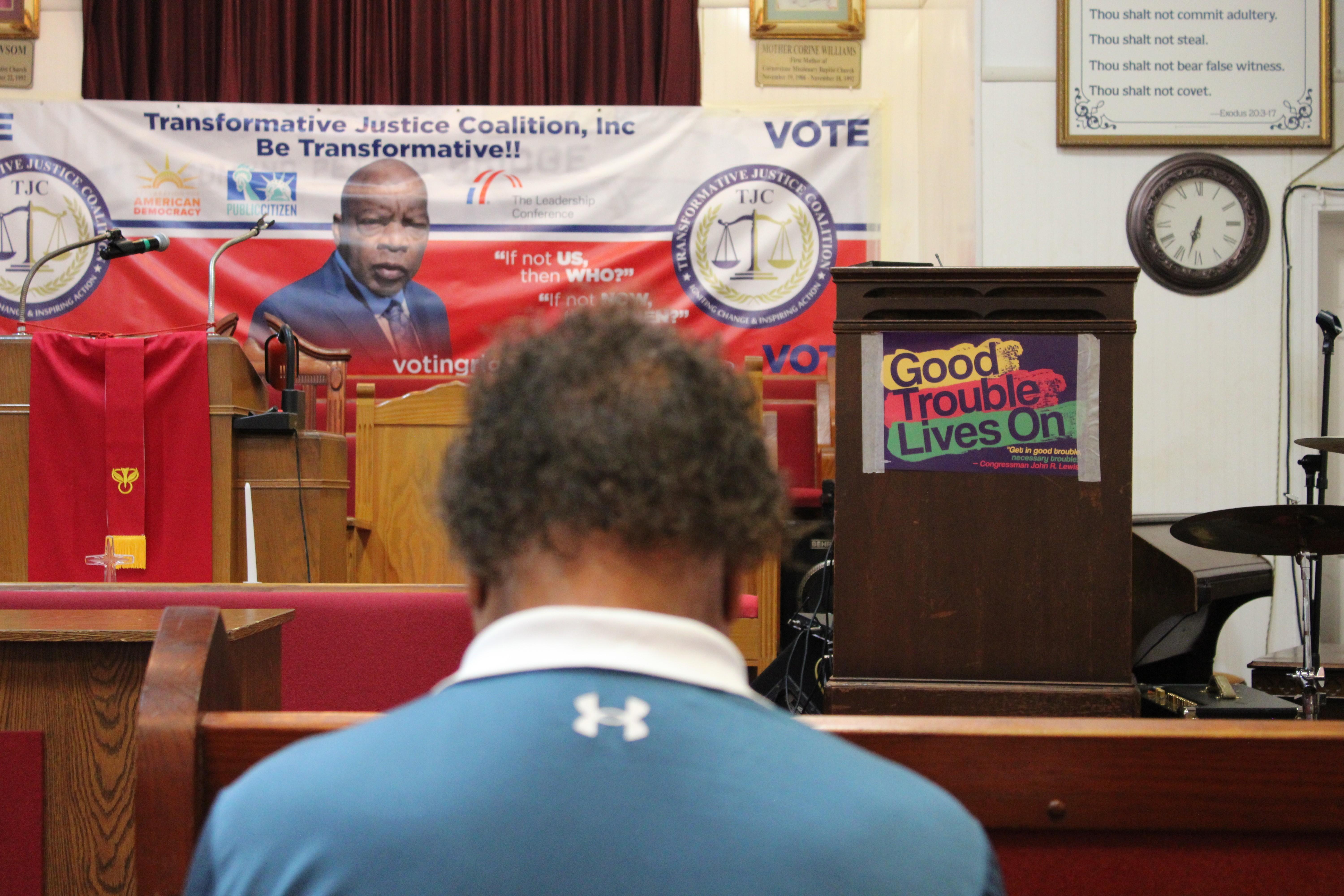 A man in a blue shirt sits with his head bowed during a church demonstration.