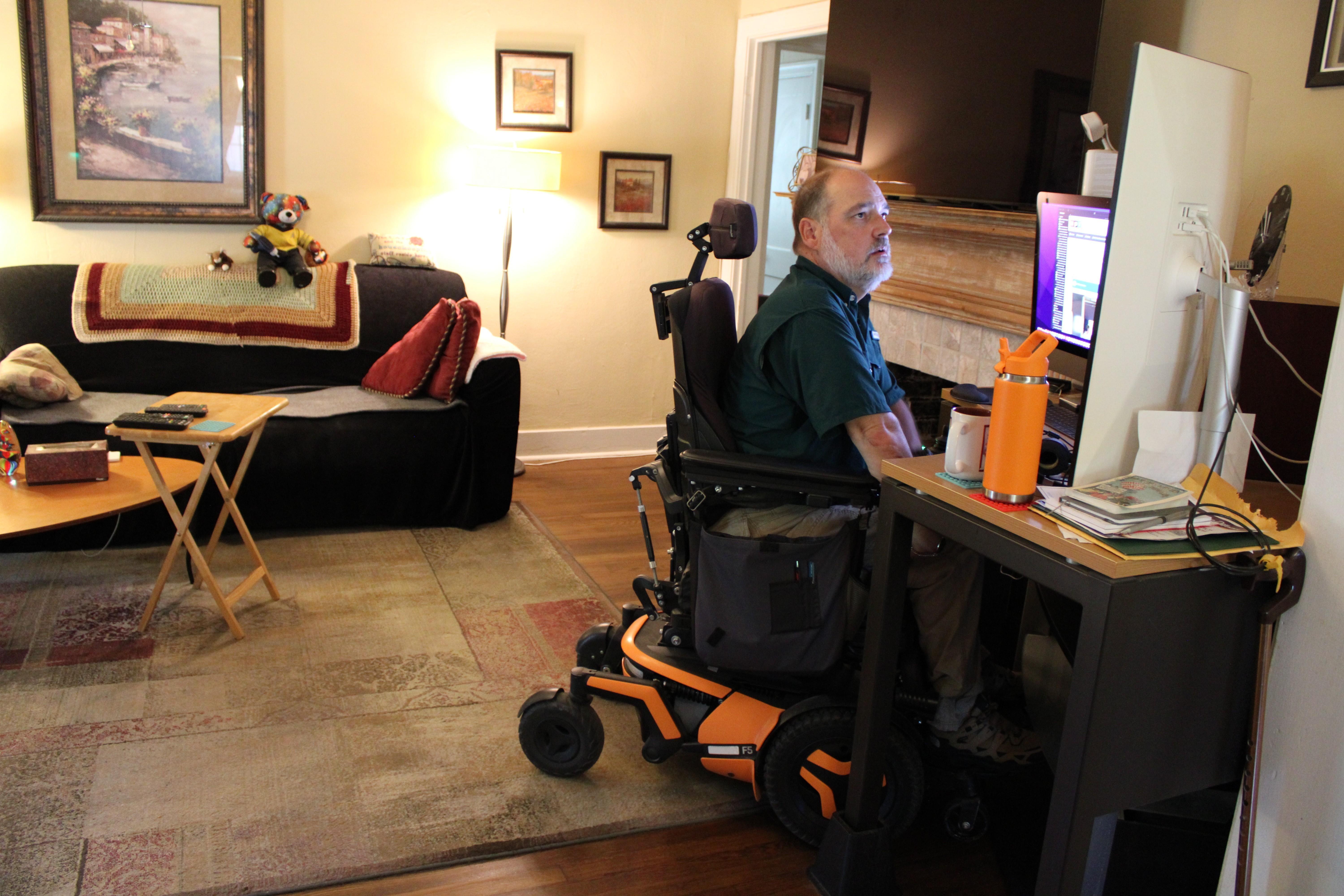 A man using an electric wheelchair looks at his computer screen