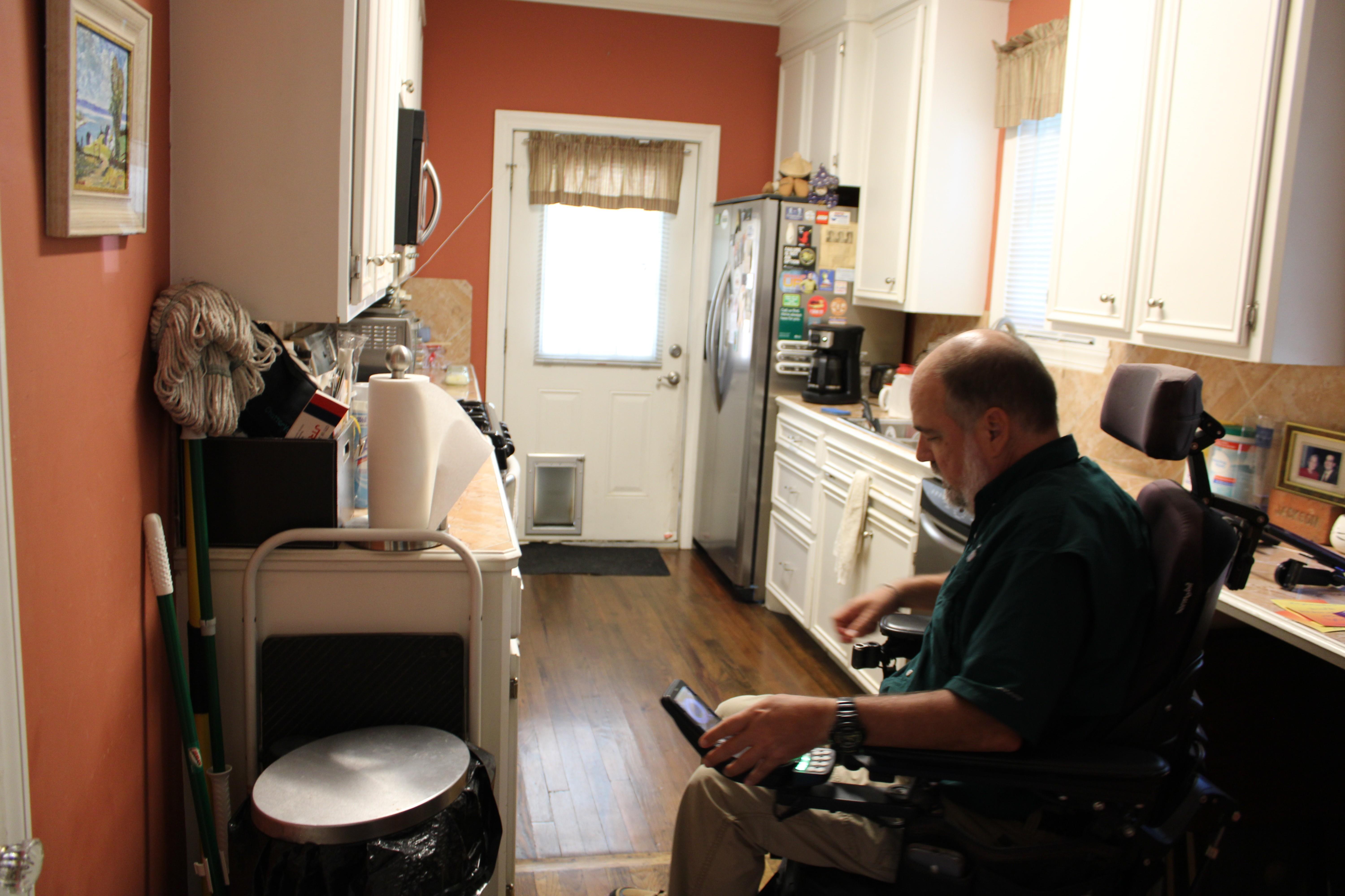 A man using an electric wheelchair tries to guide it through his narrow kitchen.