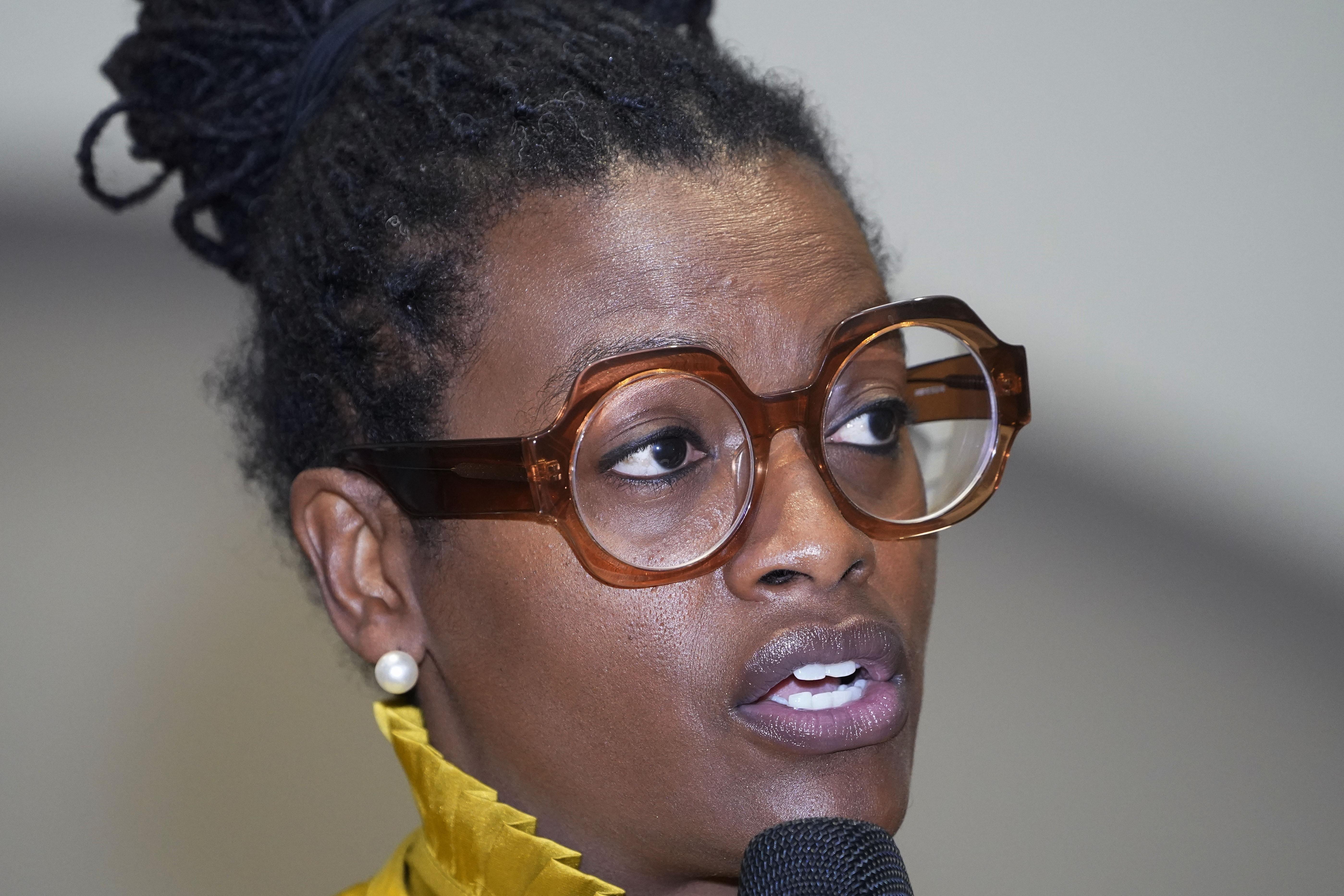 A Black woman wearing glasses and pearl earrings speaks into a mic.