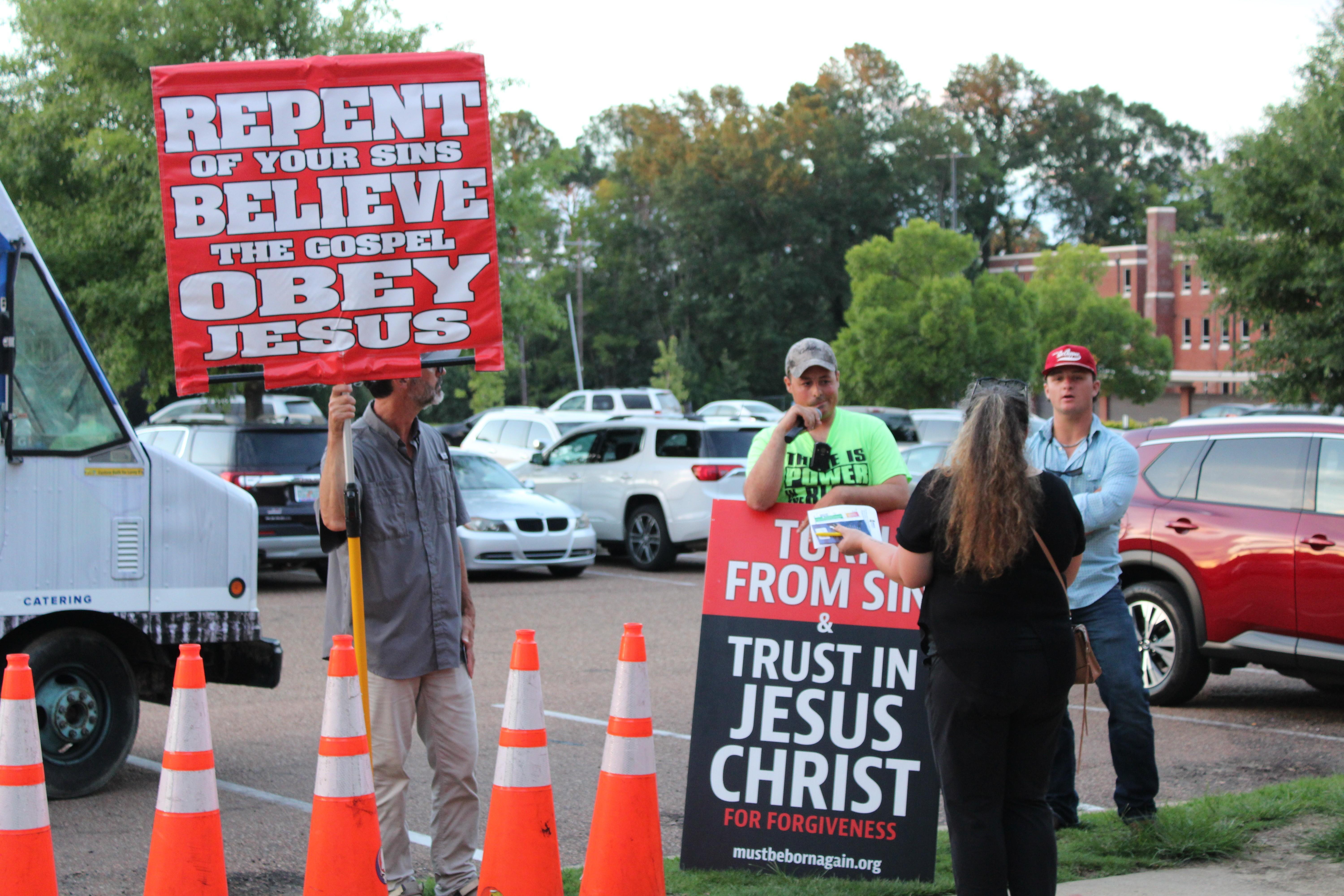 Men holding signs speak with a woman wearing black.