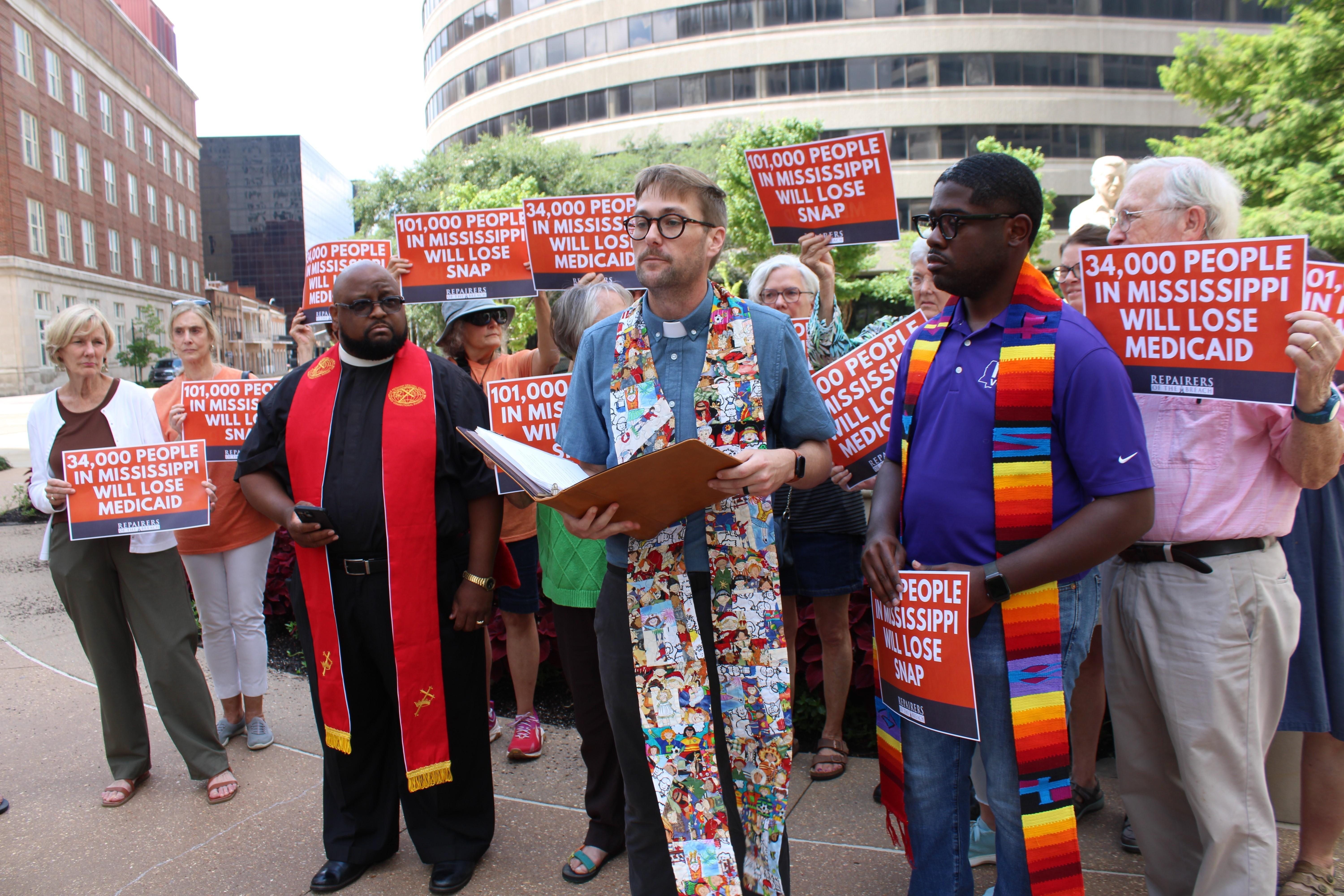 Pastors stand in front of demonstrators outside of an office building.