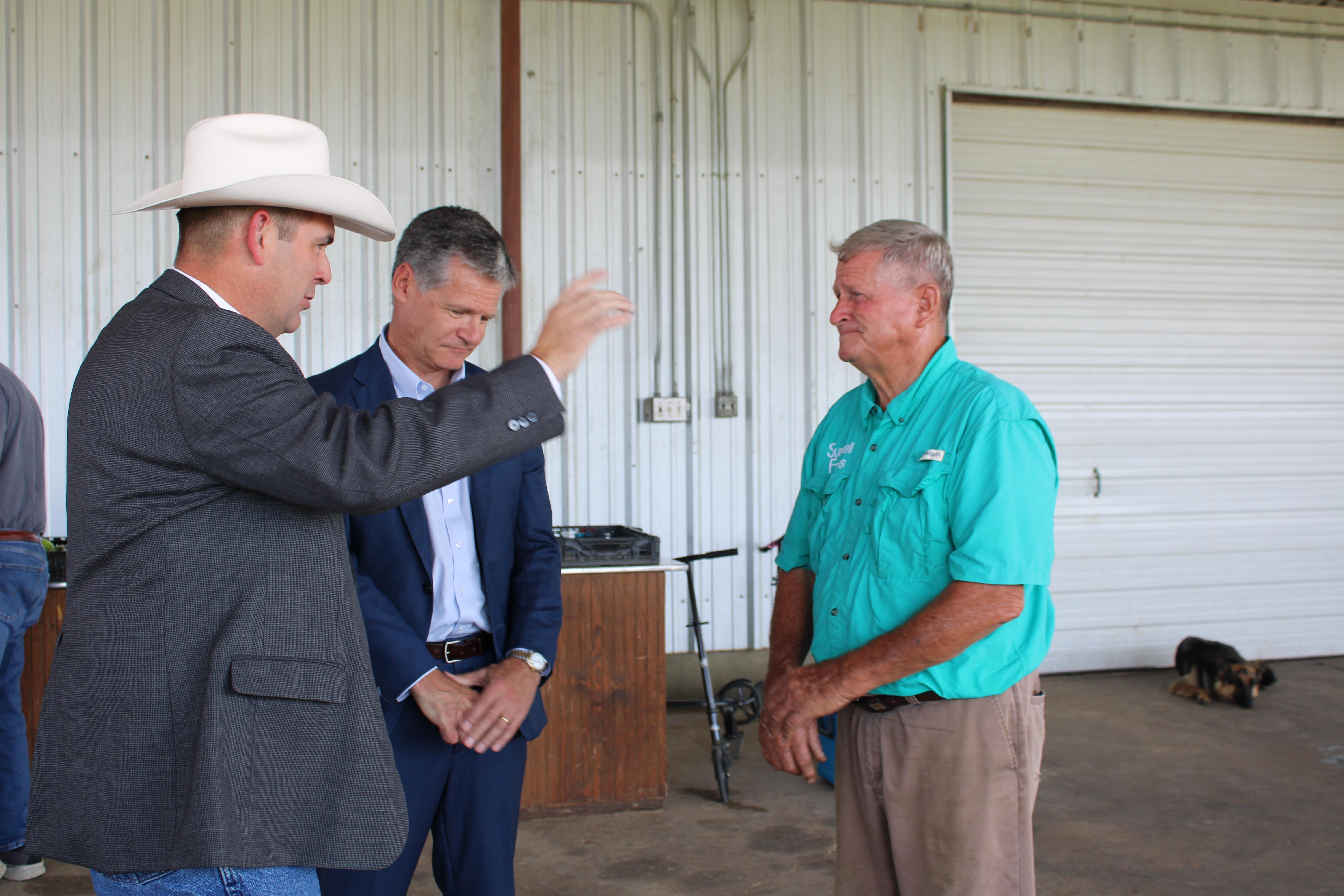 Three men talk amongst themselves at a farm.