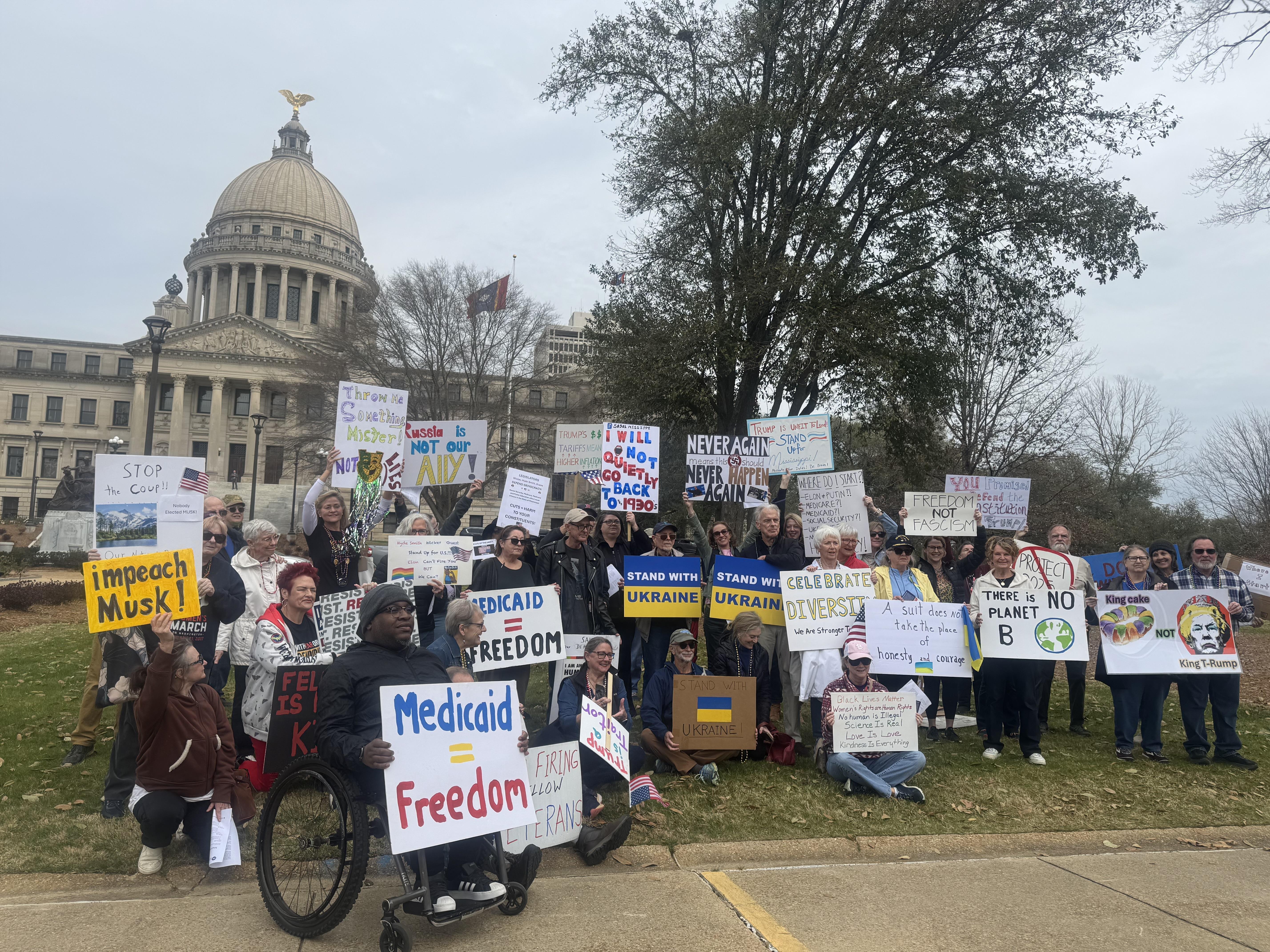 Protesters stand, kneel and sit holding signs.