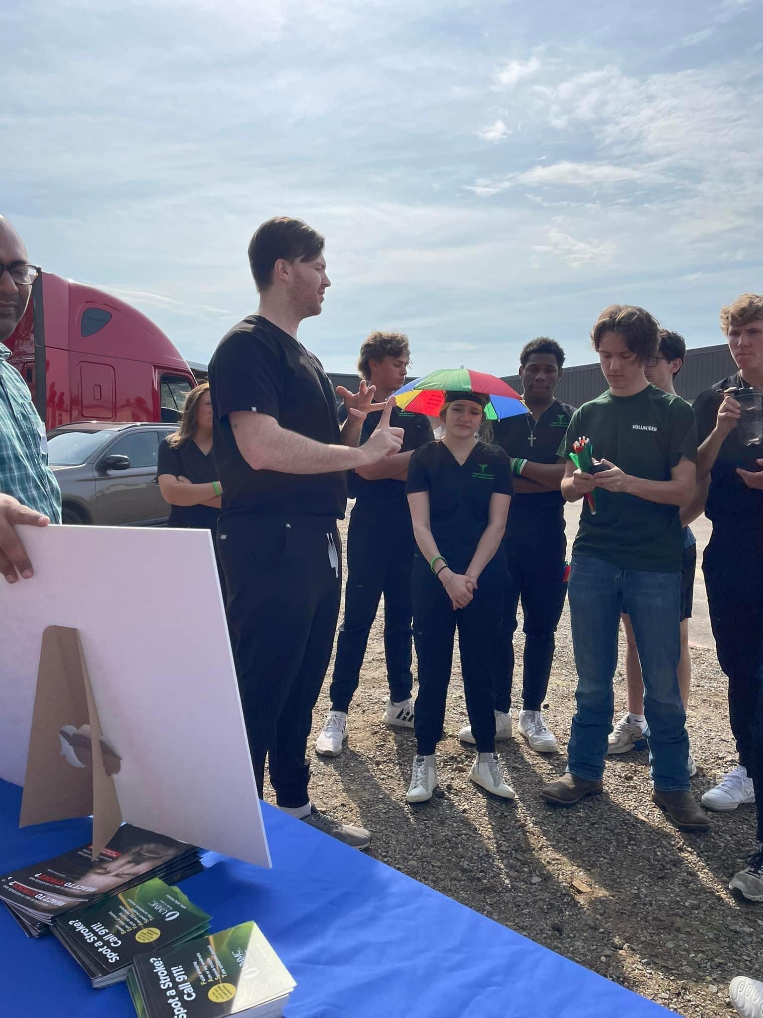 A doctor wearing black scrubs stands in front of a group of young people.