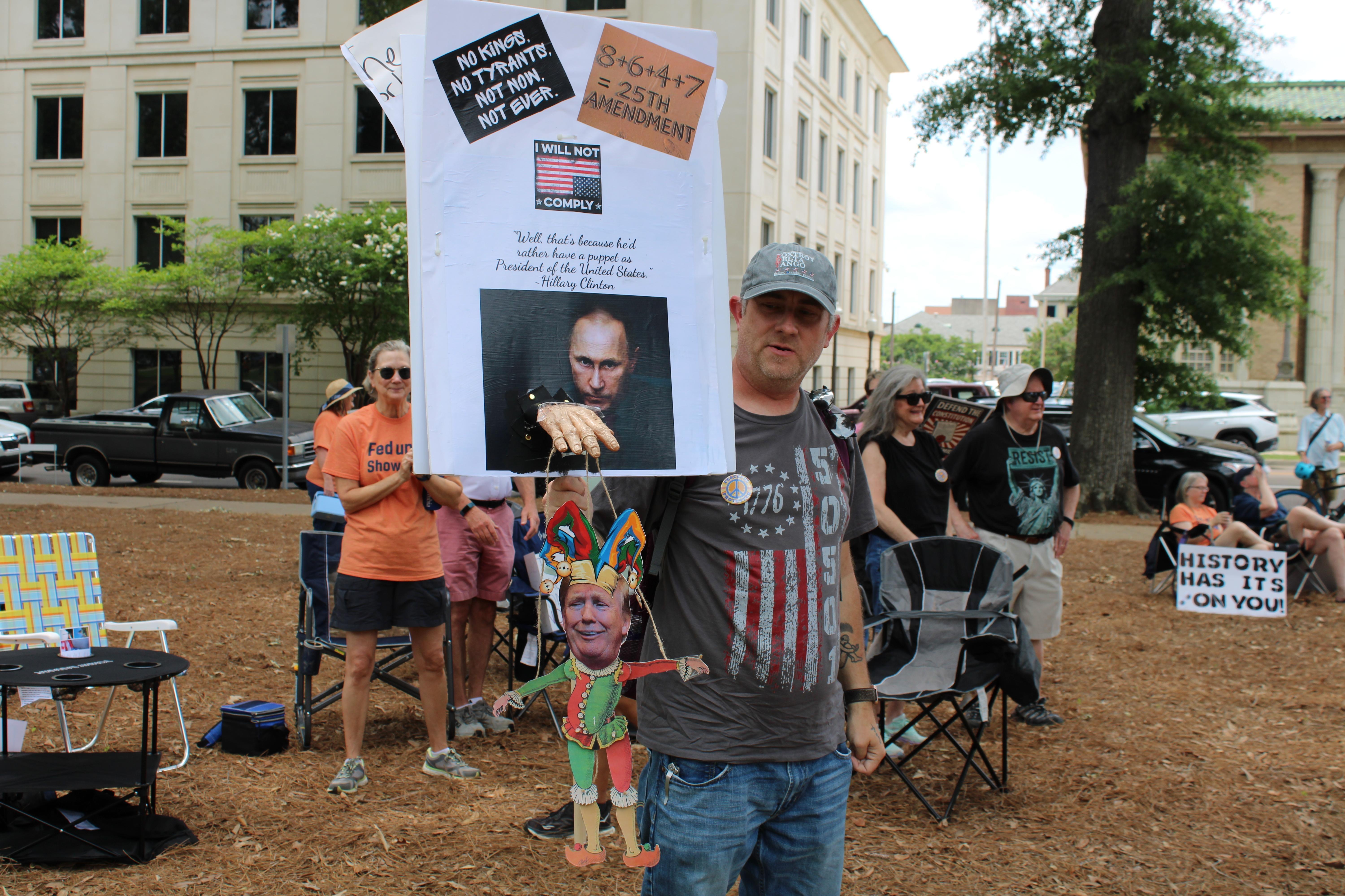 A man carries a sign featuring a puppet version of President Trump.