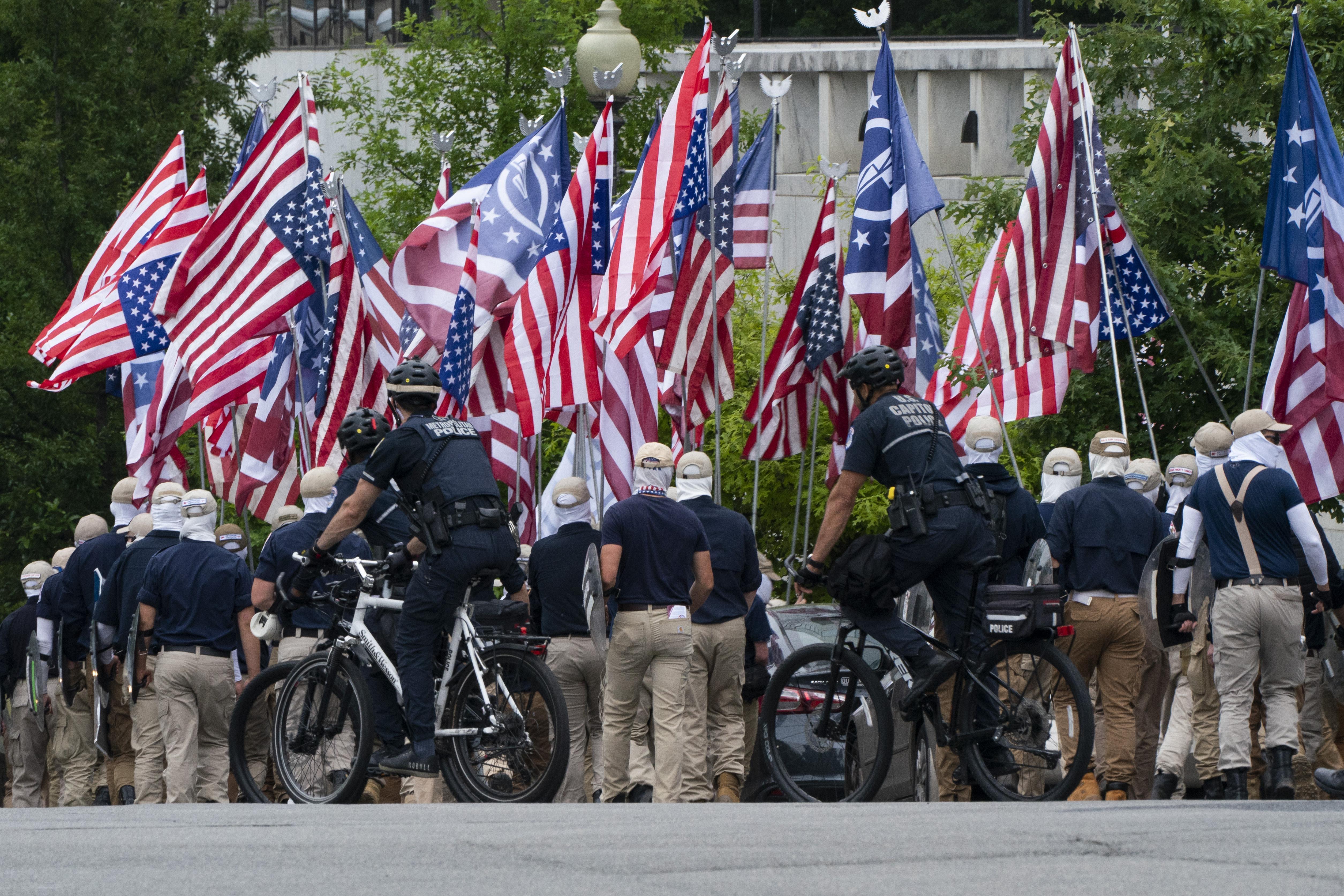 Anonymous members of a white supremacist group marches down a road in DC, shielding their faces.