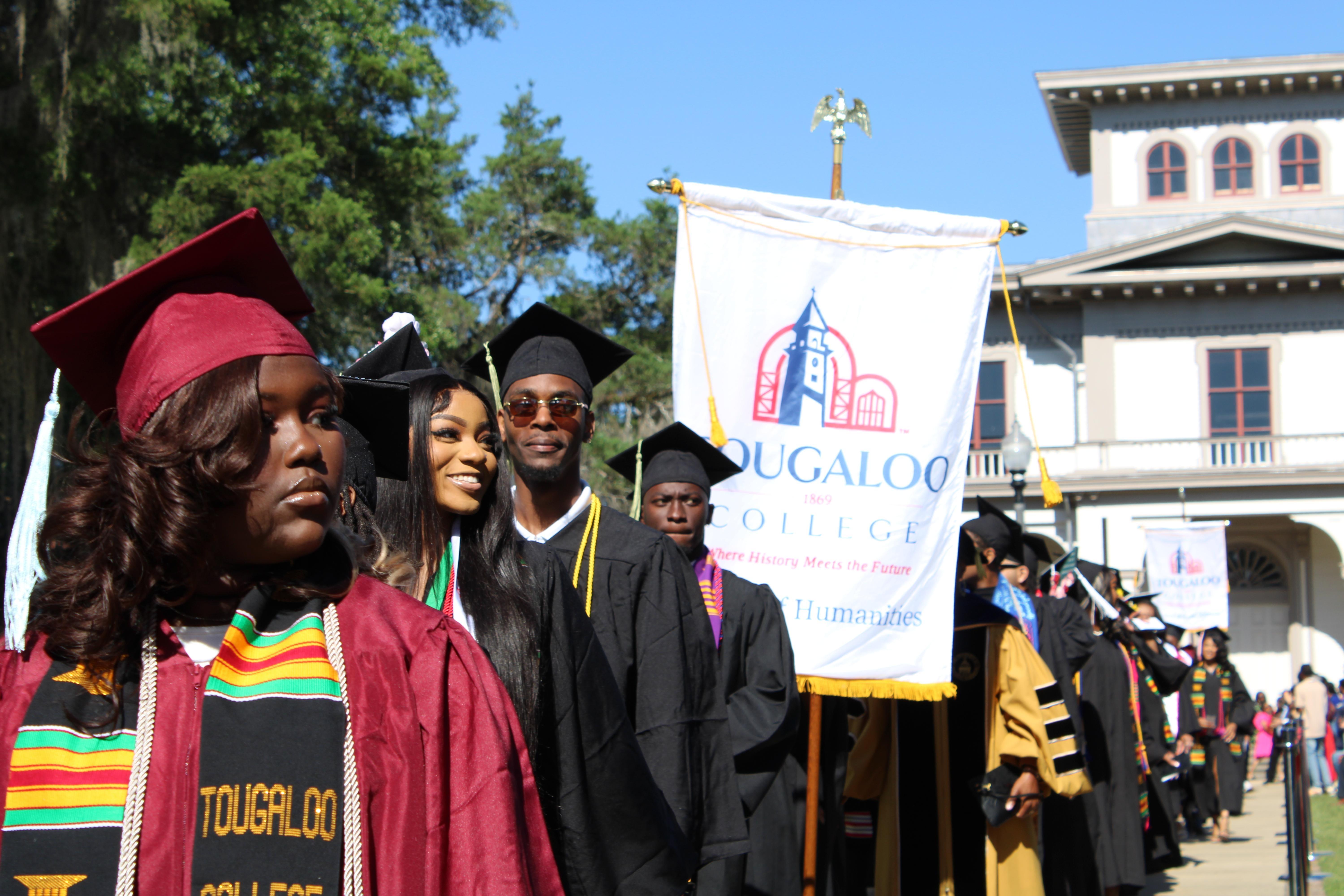 A line of graduating college students, some with kente cloth regalia, prepare to graduate.