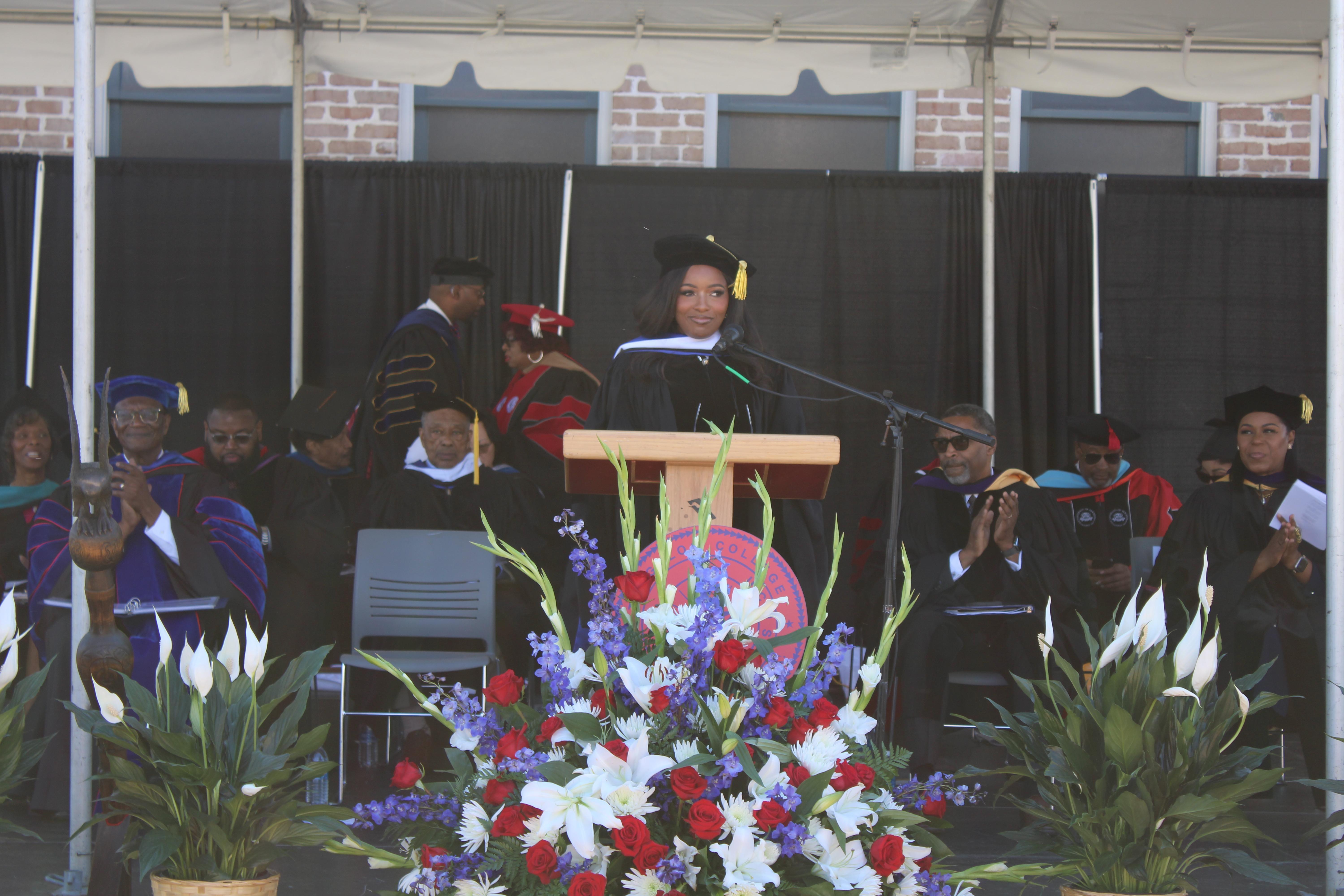A woman in graduate regalia speaks at a podium.