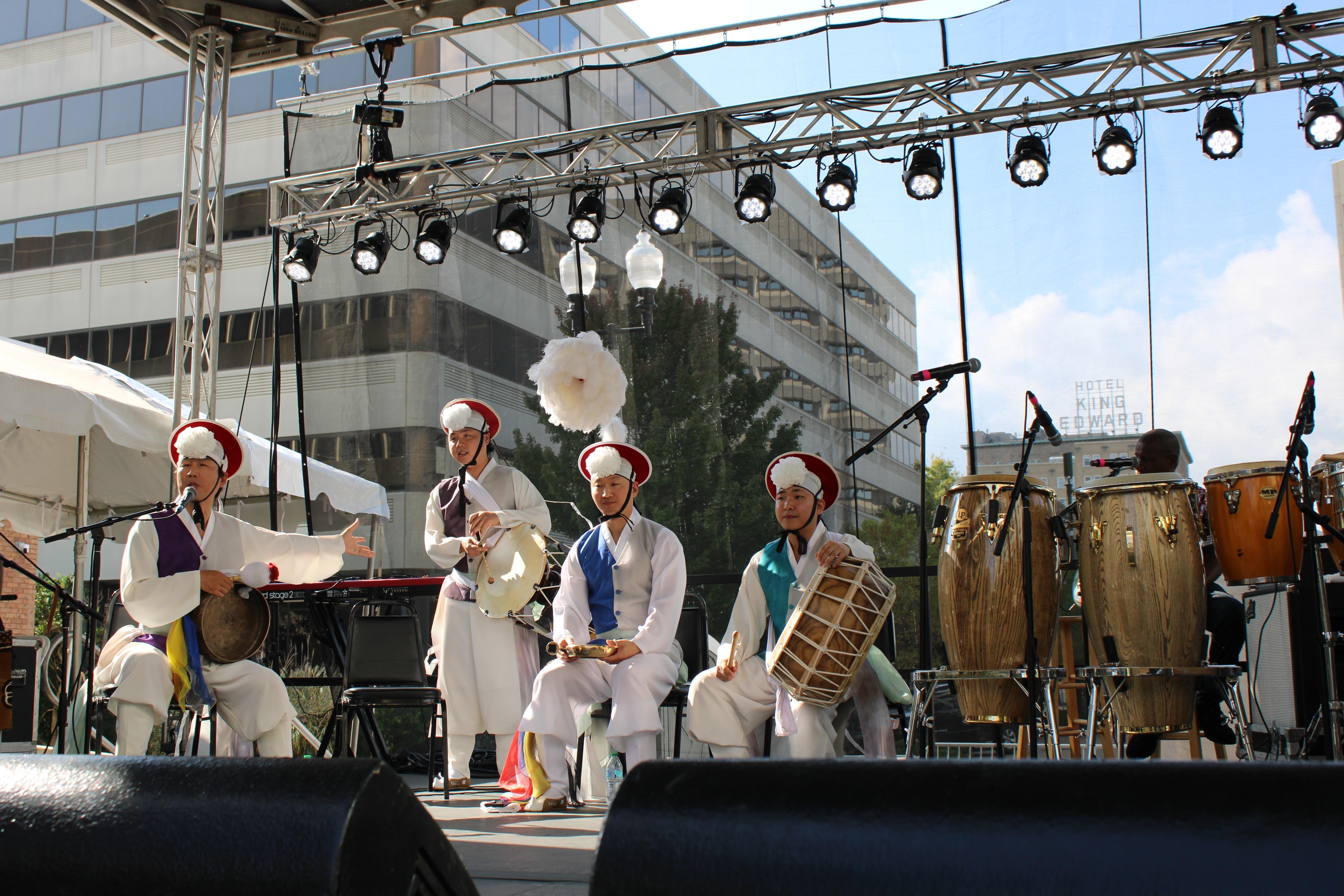 Four members of a Korean Performing Arts troupe are seen on a stage with instruments while dressed in traditional clothing.