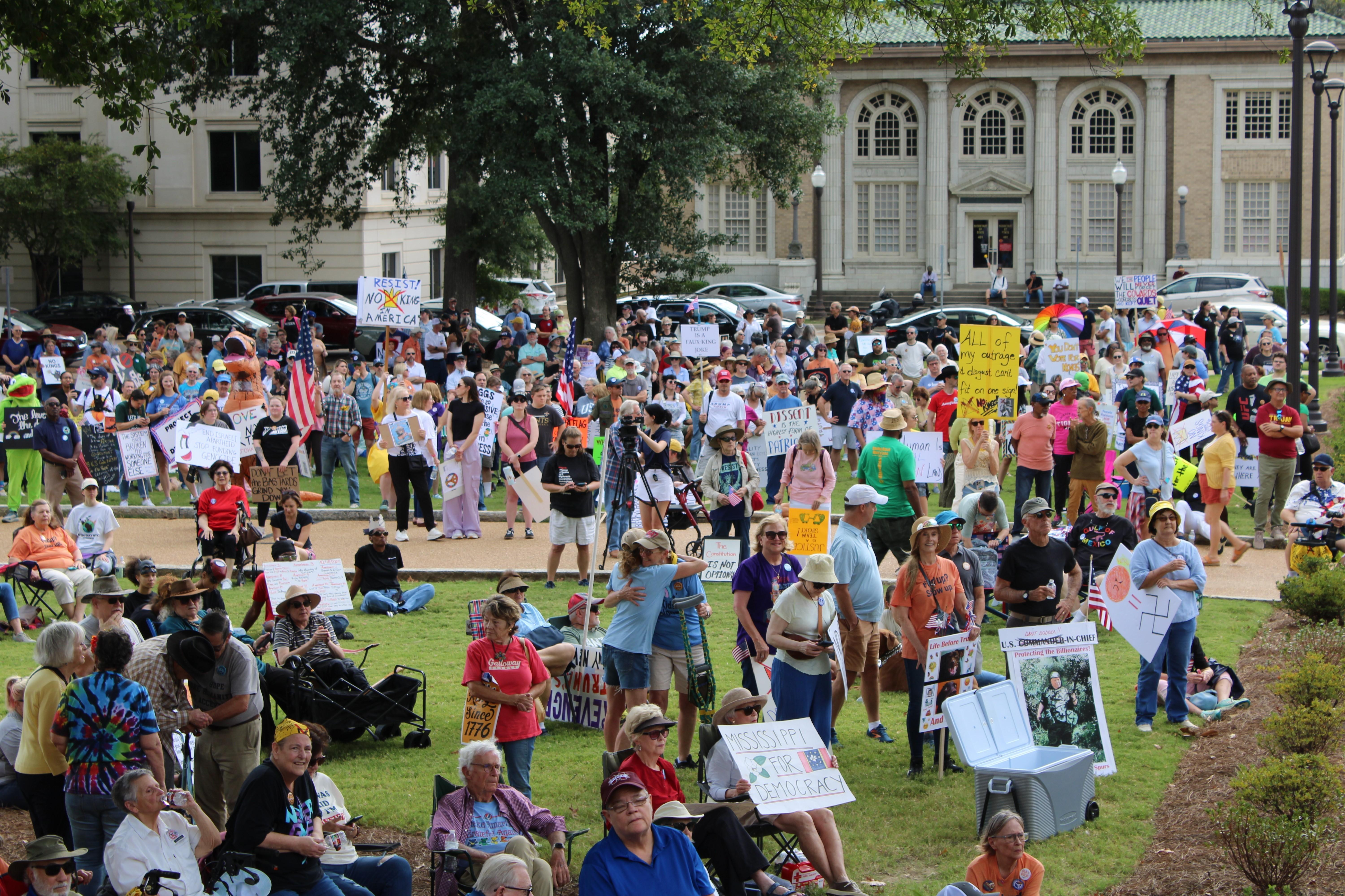 Protesters with signs sit and stand at a rally