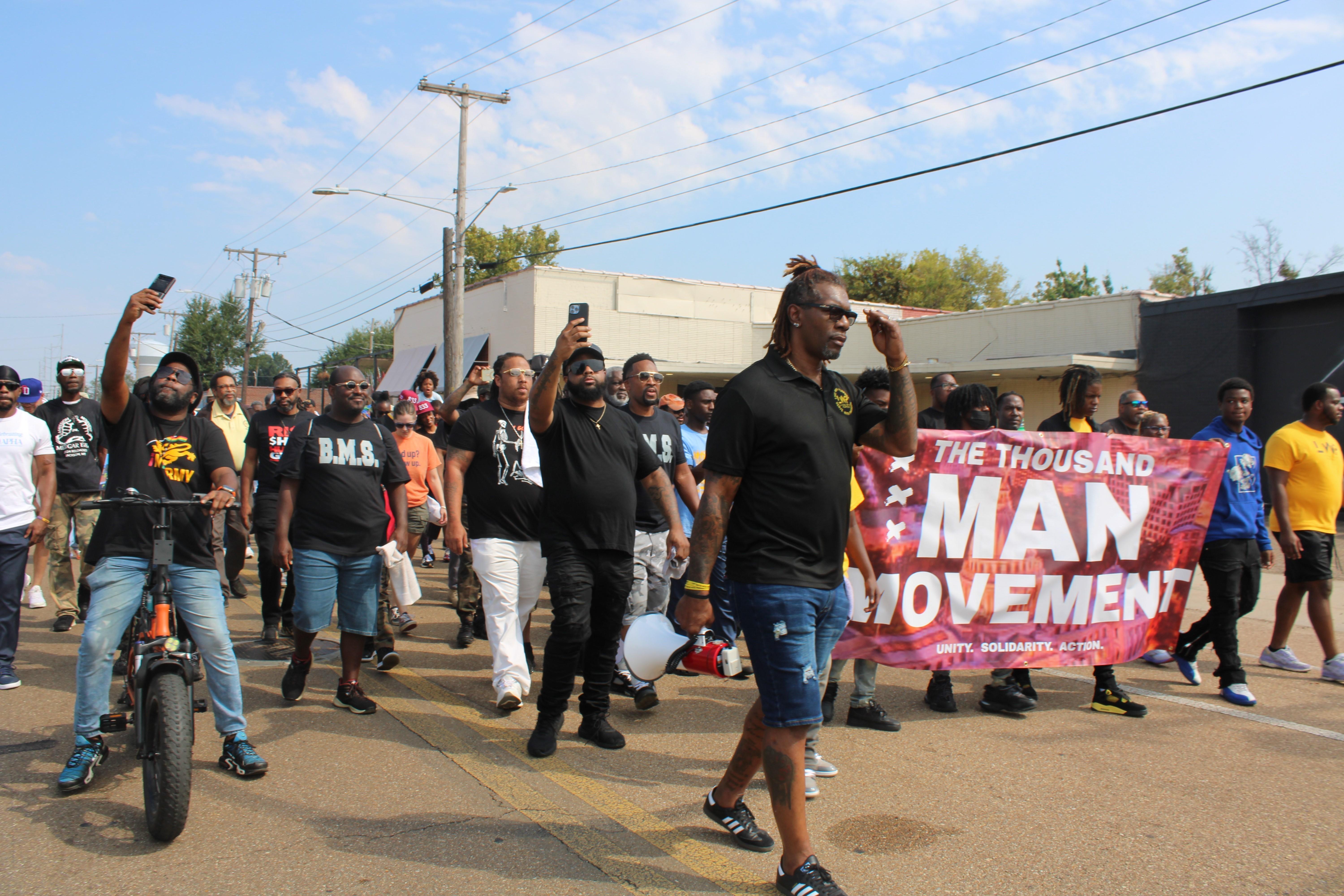 People march holding a 'Thousand Man Movement' sign.