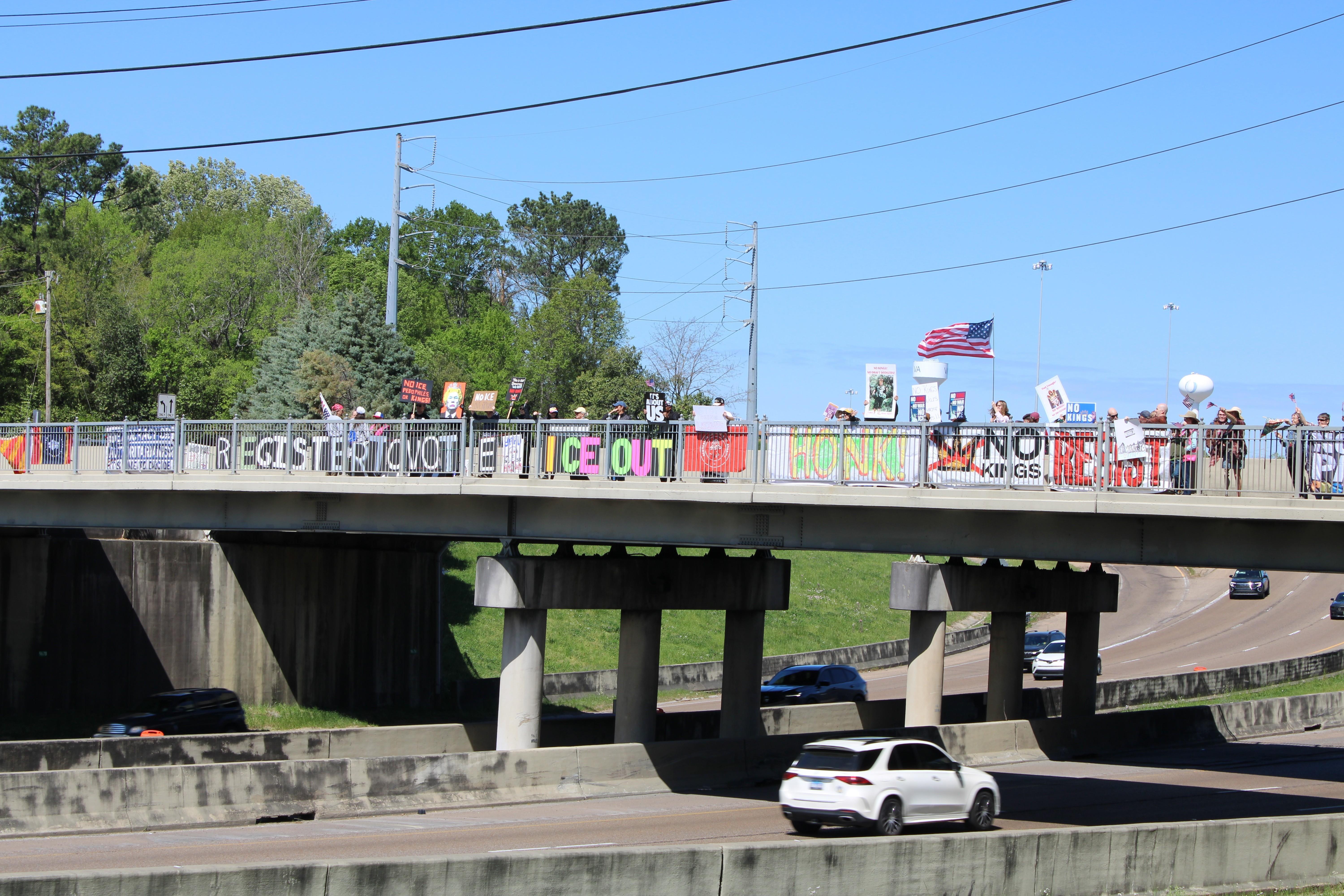 Demonstrators wave signs on the Museum Hiking Trail bridge overlooking I-55 in Jackson.