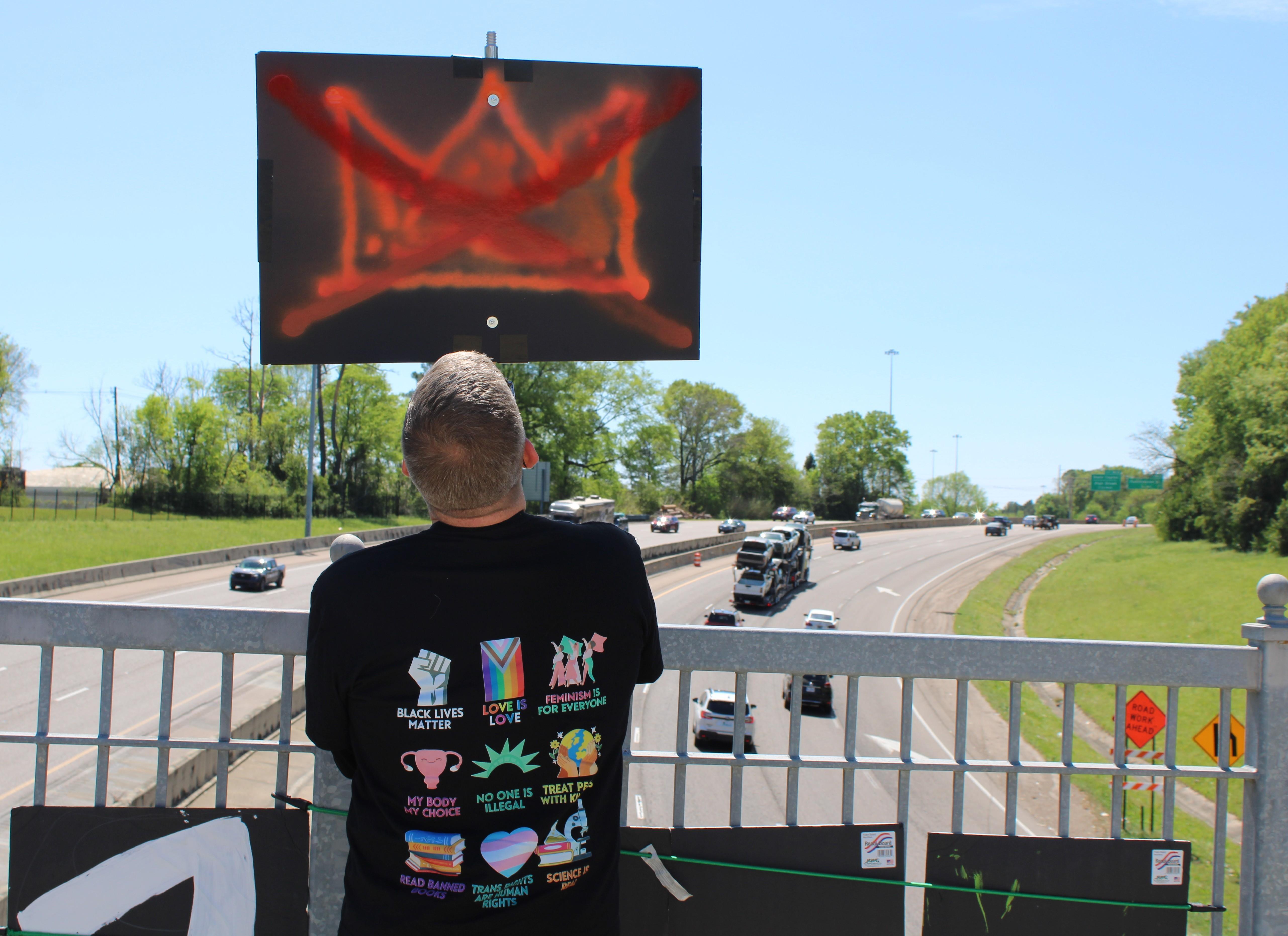 A demonstrator holds a sign on the Museum Trail bridge in Jackson during a 'No Kings' rally.