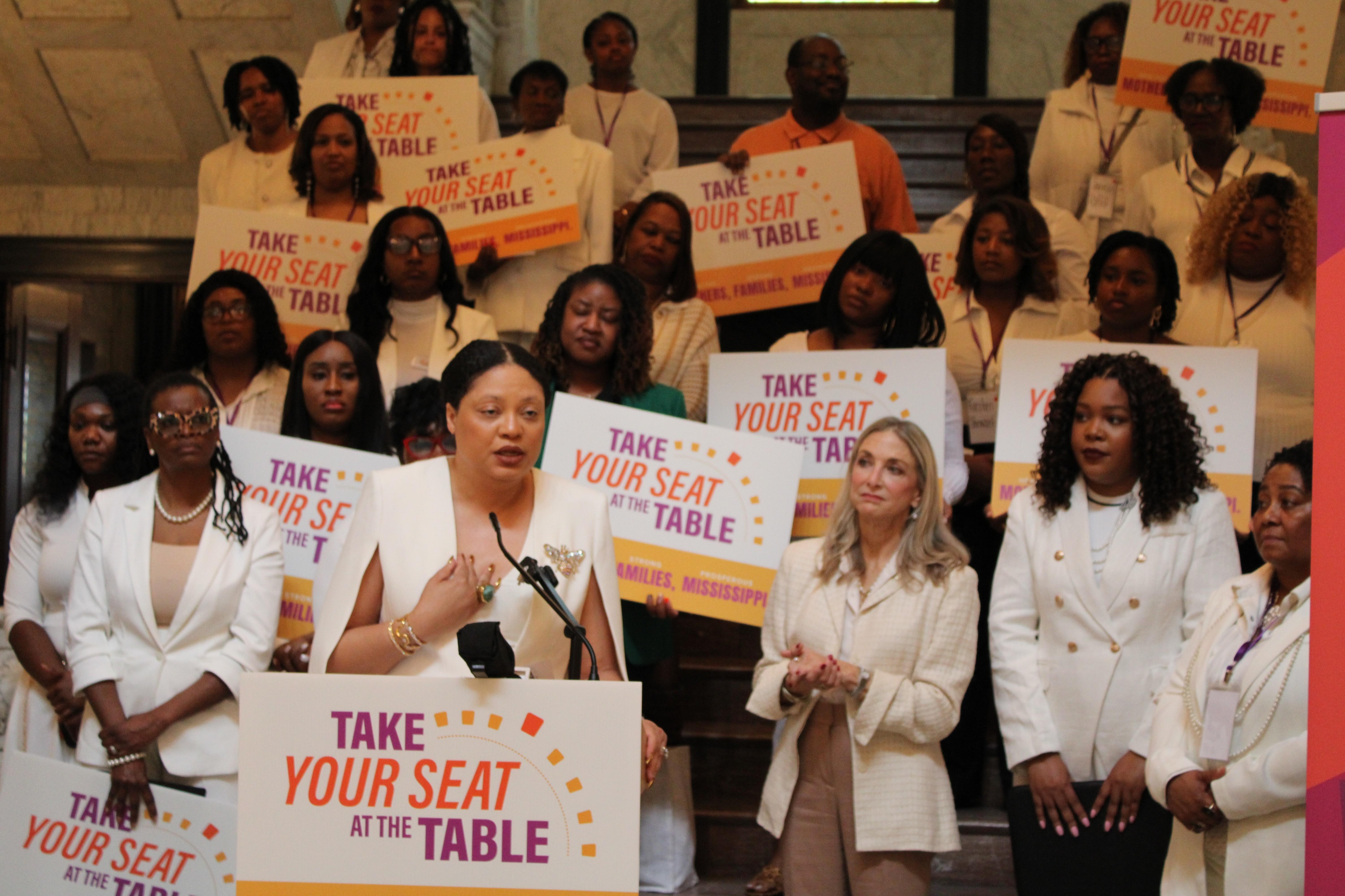 Certified Professional Midwife Tanya Smith-Johnson speaks during the Mississippi Black Women's Roundtable advocacy day dressed in white and with other women dressed in white behind her.