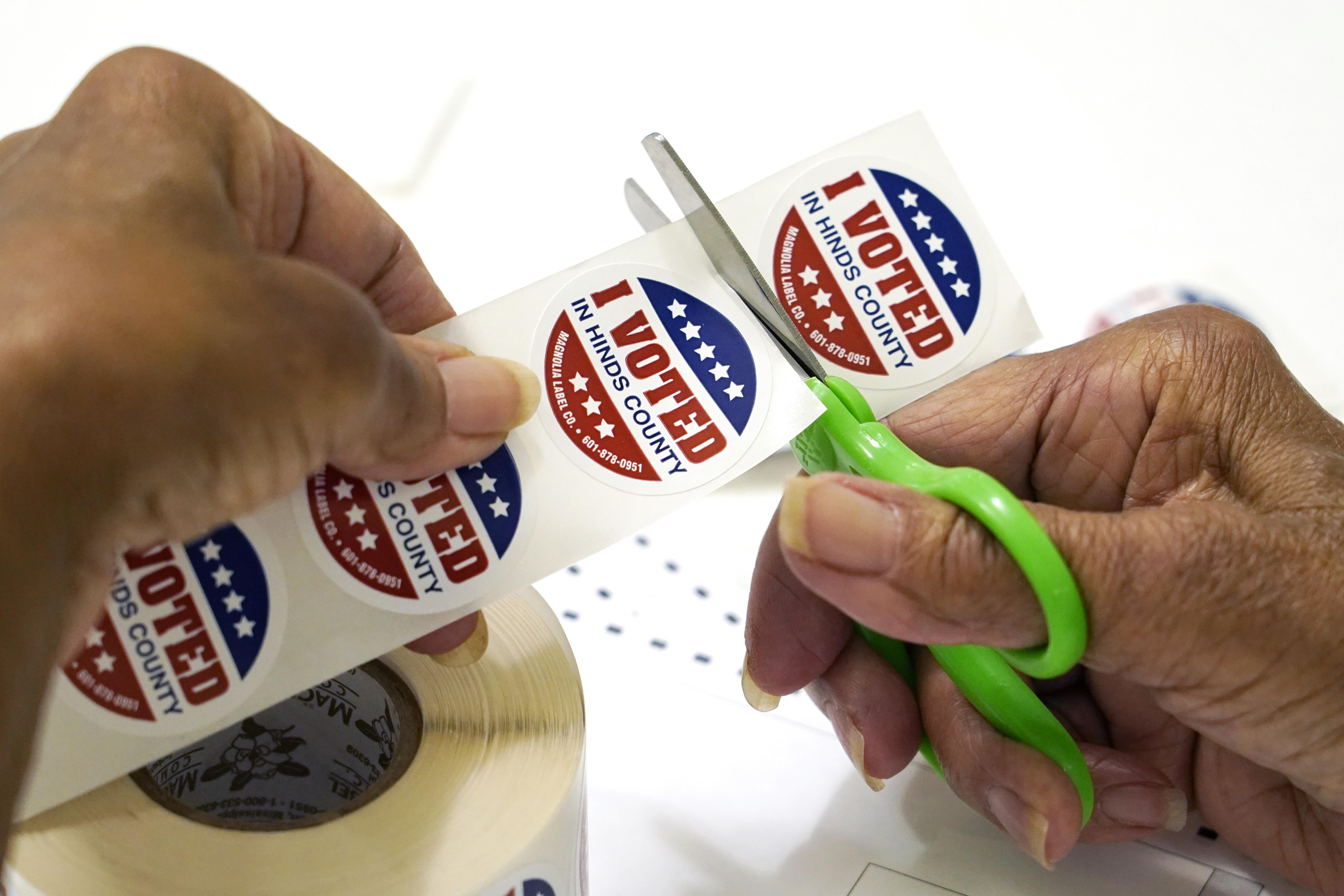 A precinct worker in Jackson, Miss., cuts individual "I Voted in Hinds County" stickers from the roll, Aug. 8, 2023. 