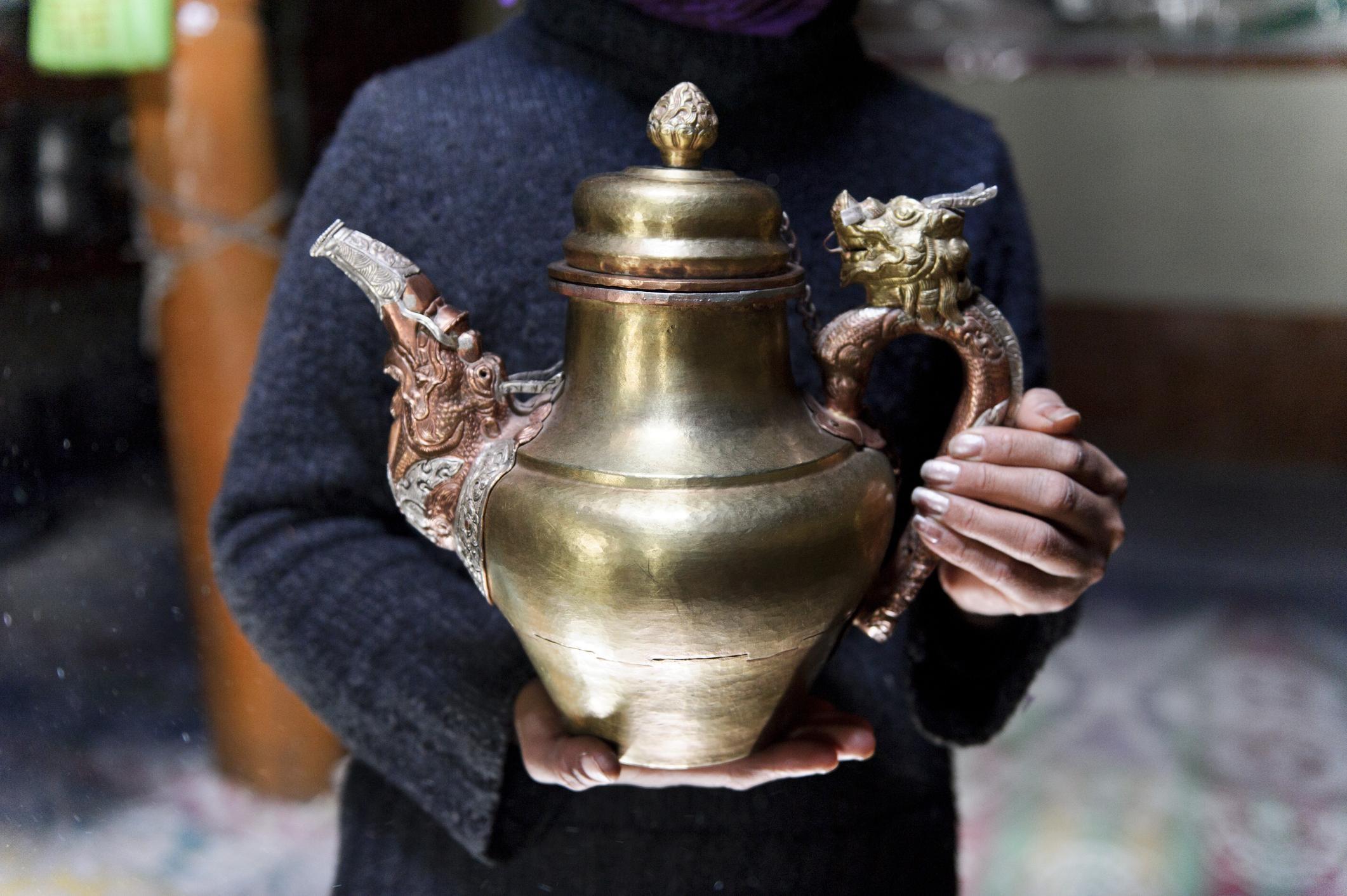 woman holding a large silver teapot with dragon details