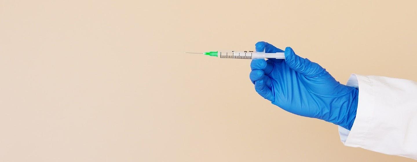Person with a blue latex glove on holds a syringe