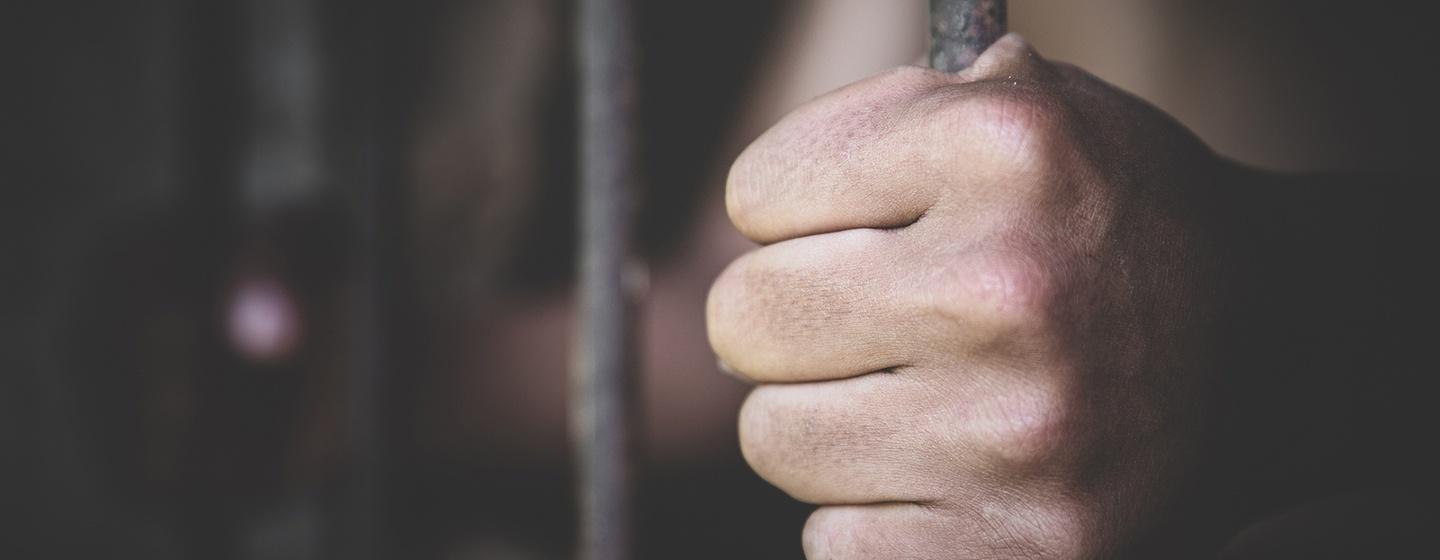 Stock photo of hand on prison cell bars