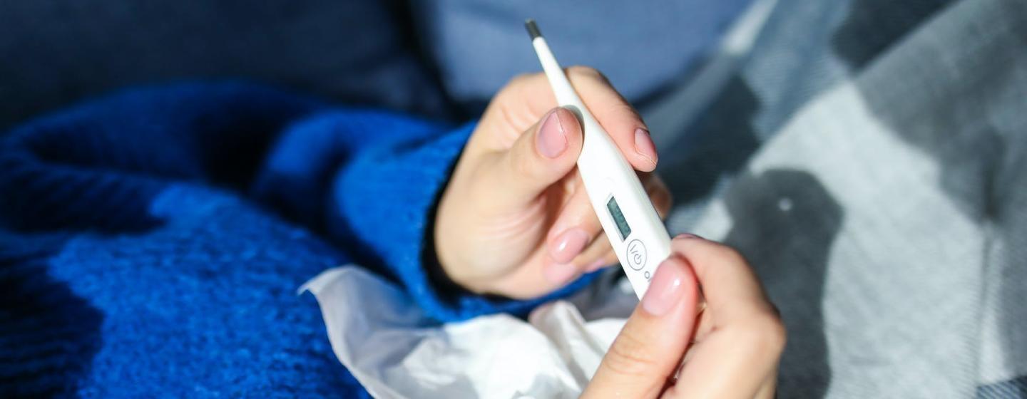 An individual checks their body temperature with a medical thermometer