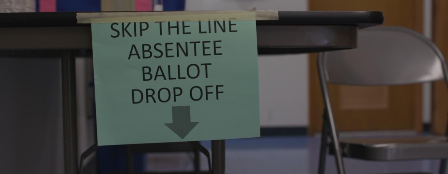Sign taped to a table that says "skip the line absentee ballot drop off"