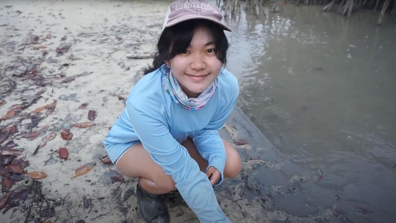 Show host Cara Lin is sitting on the wetlands of a Guam shoreline jungle