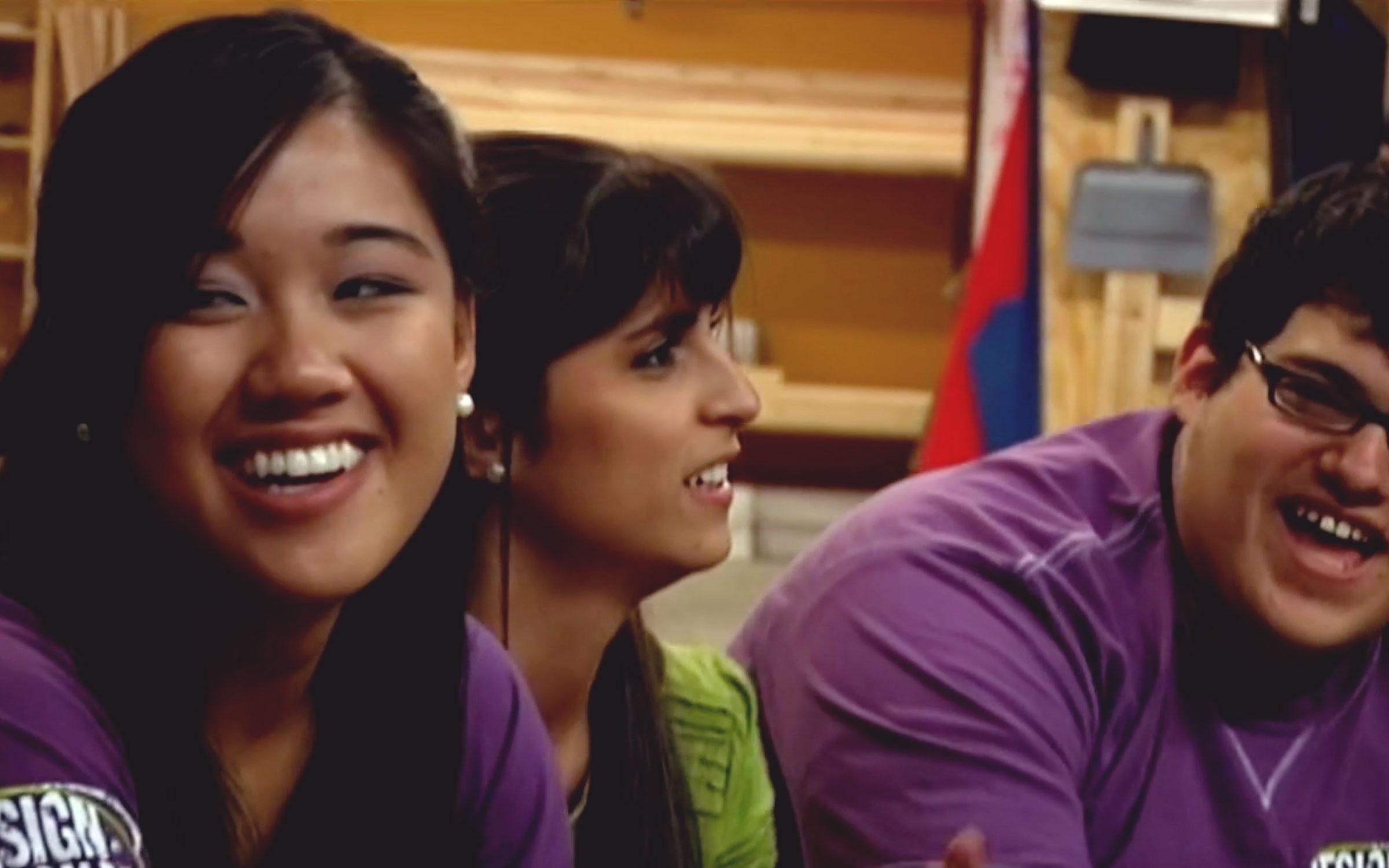 Two female teens and one male teen laugh among themselves in a classroom