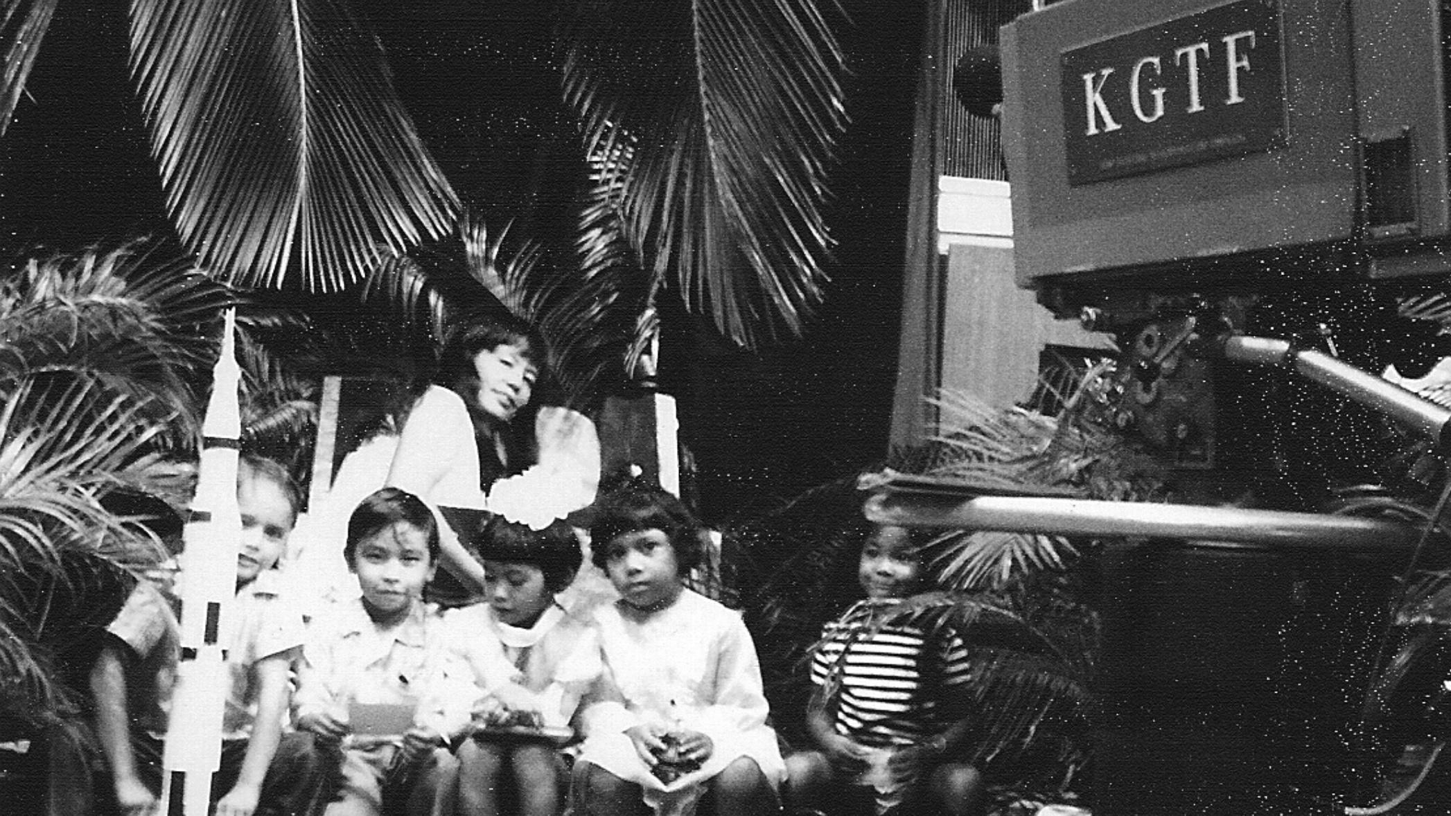 A black and white photo of kids holding their toy rockets next to the host in front of old KGTF television cameras