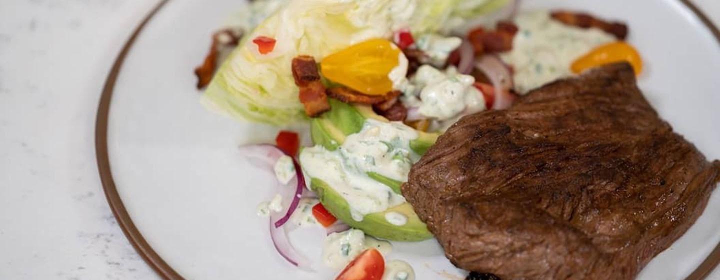 Buttermilk steak on plate alongside wedge salad with dressing