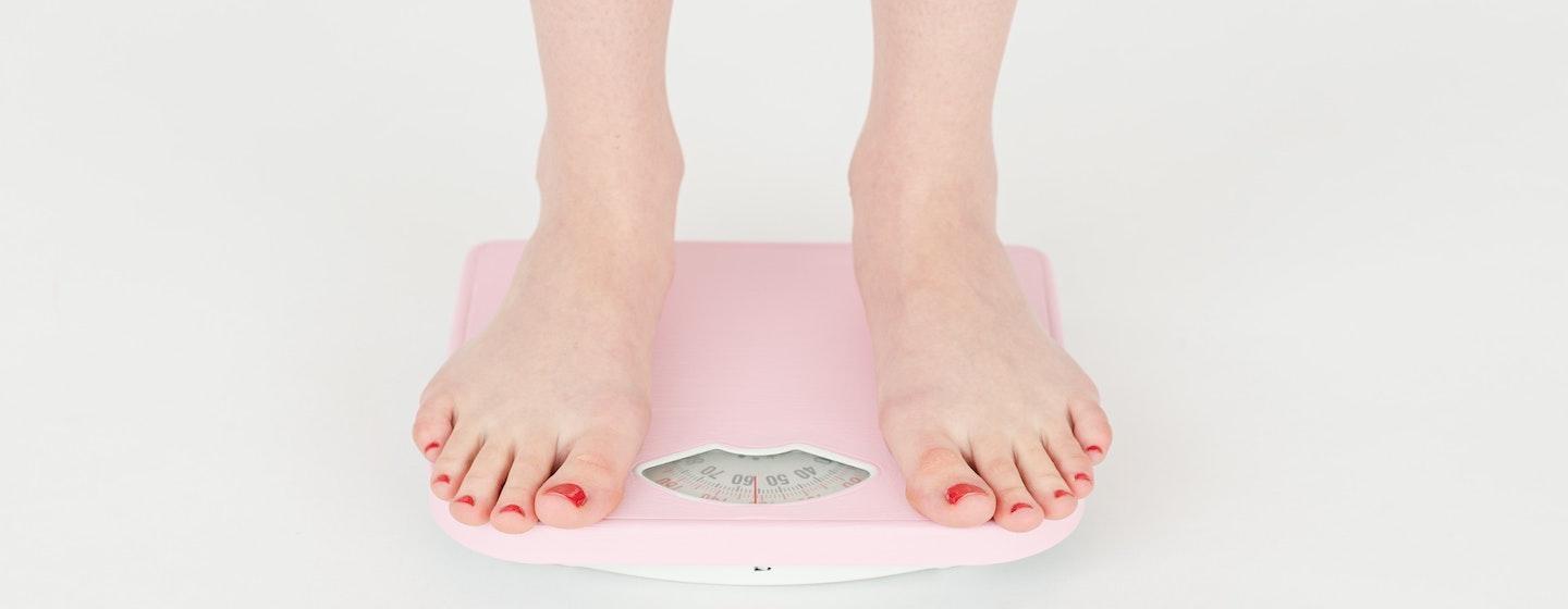 woman with red painted toe nails standing on weigh scale, losing, gaining weight measurement pounds