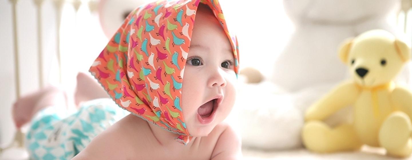 infant baby smiling talking in orange kerchief bonnet white minimalist background baby crib 