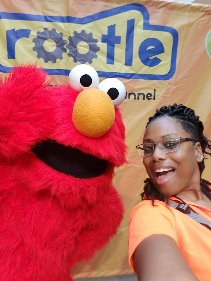 Jewel Lowe poses with Elmo in front of a Rootle banner