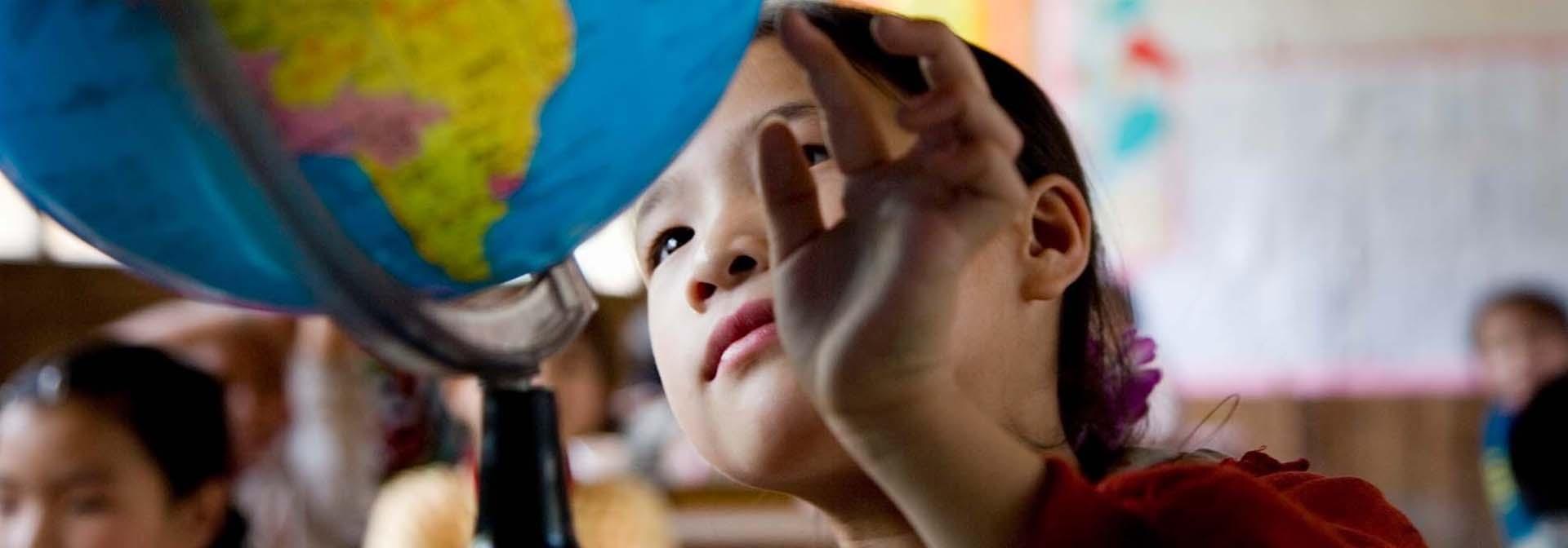 A young girl examines a globe in her classroom