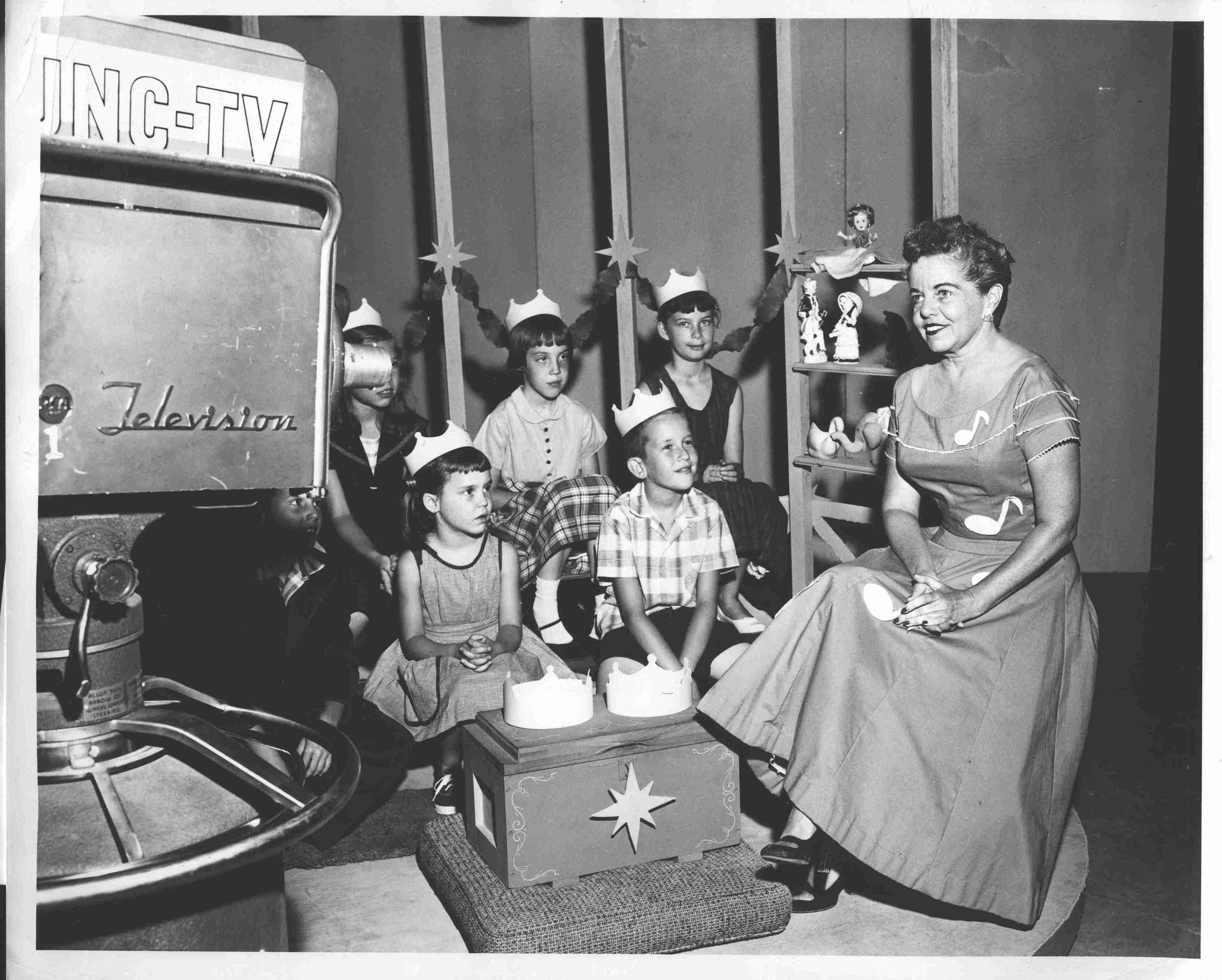 A group of children and Dottie in front of a camera on the set of Miss Dottie’s Music Box from the 1960s.