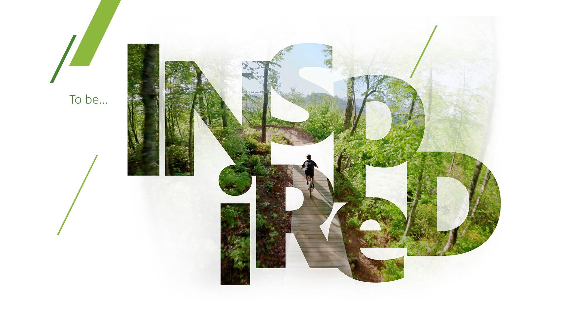 Block letters spelling out "INSPIRED" with an image of a bicyclist on a trail. within them.