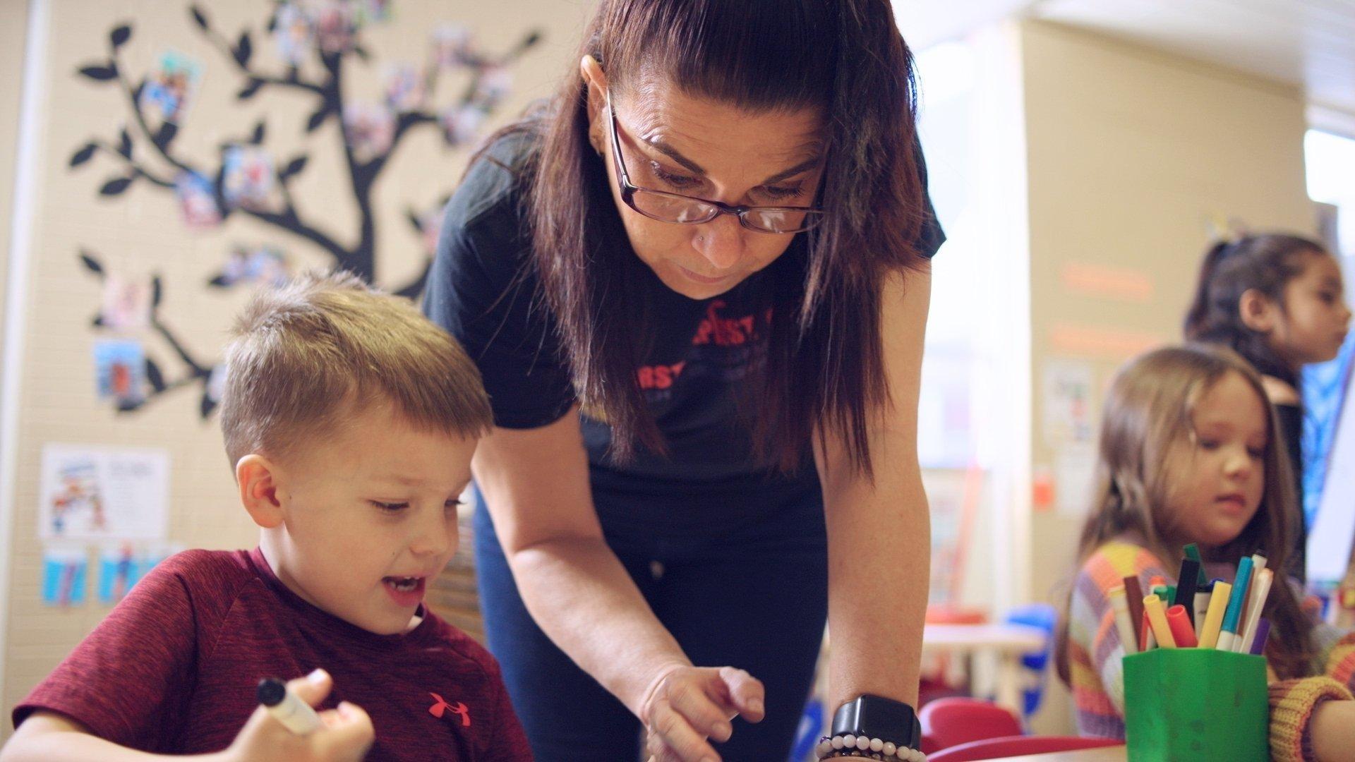 A Rootle Ambassador looking over a child's shoulder at their work.