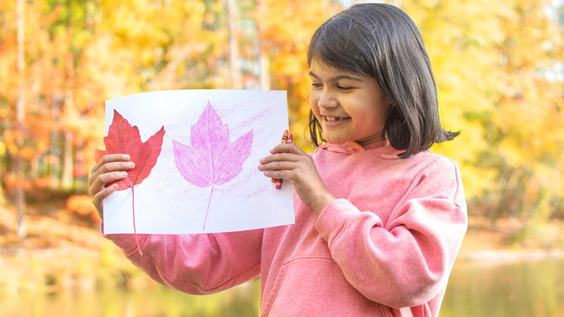 A young child about 8 years old holds up a color drawing of autumn leaves