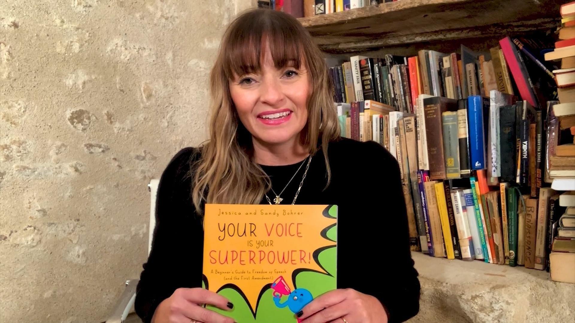 A white woman hold up a copy of the children's book, "Your Voice is Your Superpower."