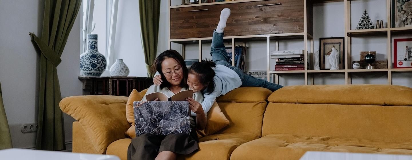 A mother and daughter at home look at a notebook on a mustard yellow couch