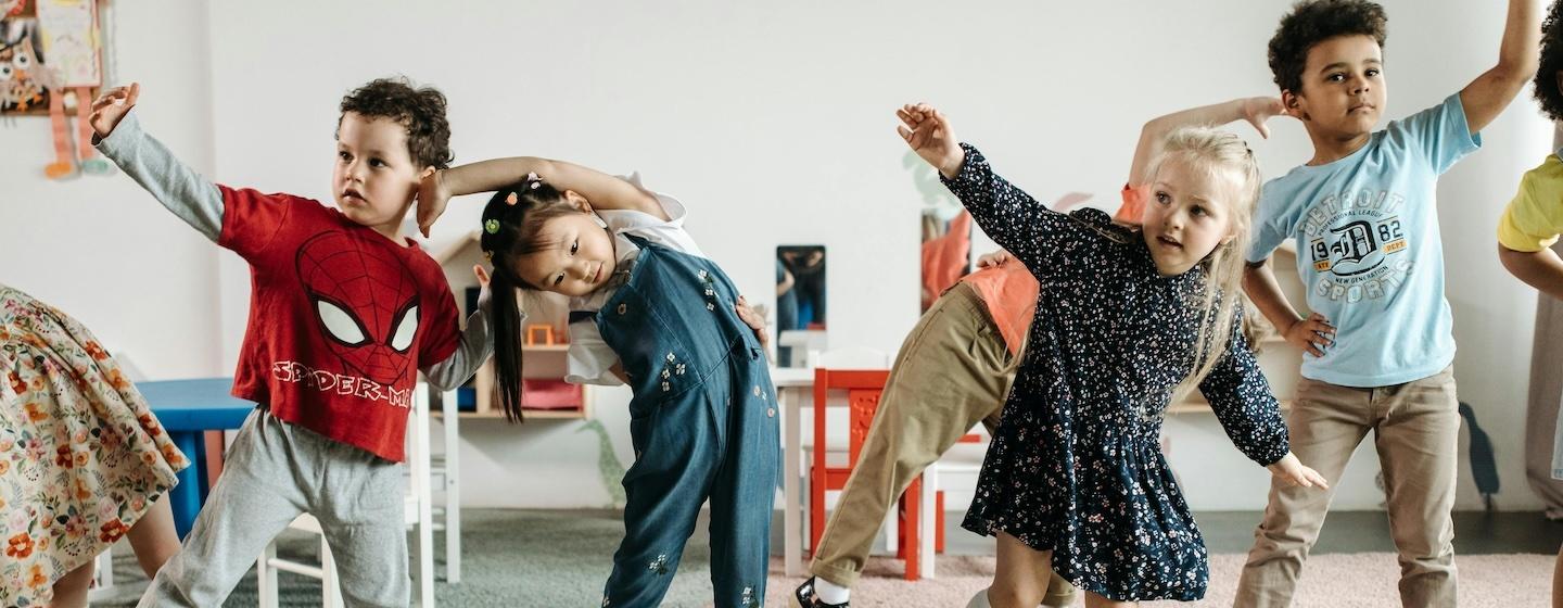 Children stretching with their arms up in a classroom setting.