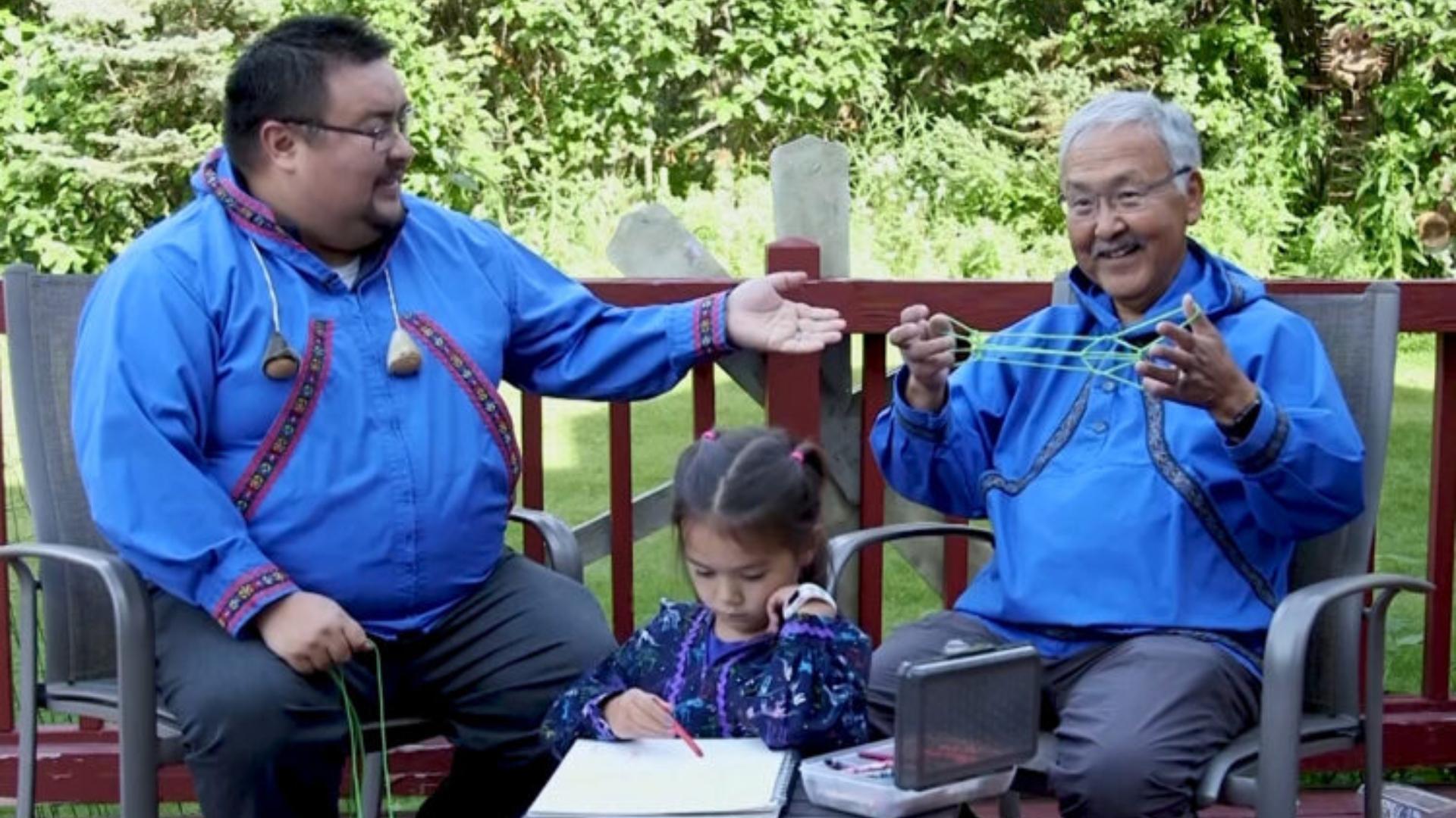 Three generations of native Alaskans doing crafts on a porch outside.